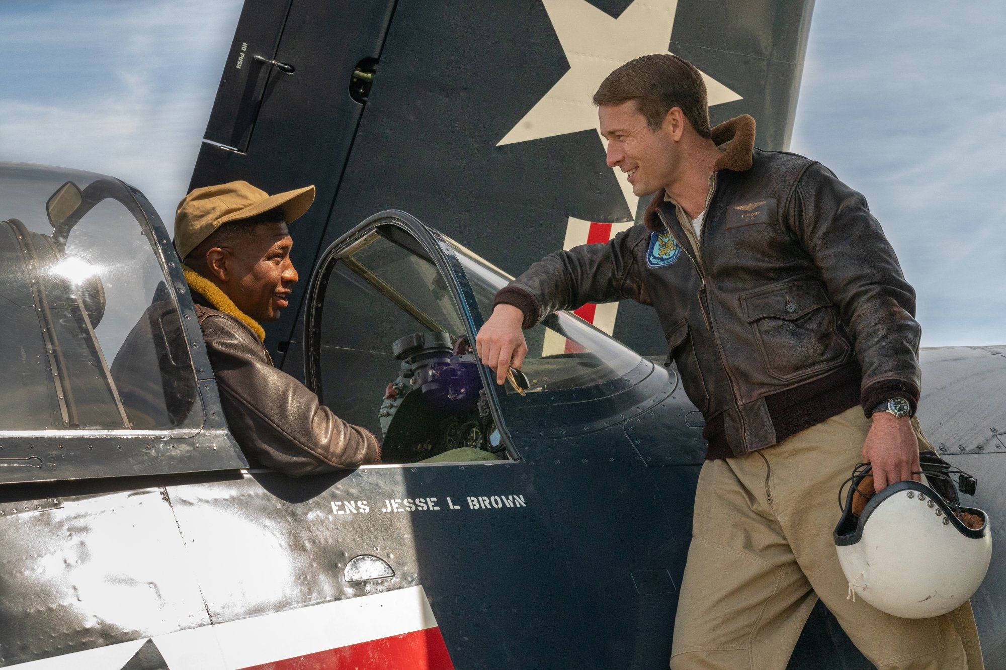 'Devotion' Jesse Brown (Jonathan Majors) and Tom Hudner (Glen Powell). Majors is sitting in the jet, while Powell is leaning against the glass shield, talking to him.