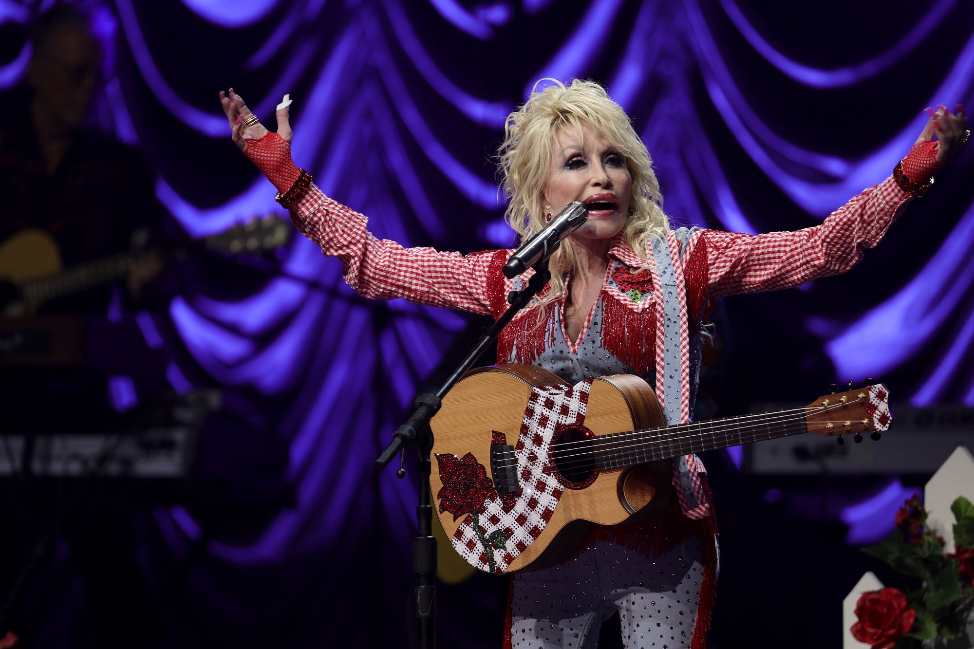 Dolly Parton performs raises her arms onstage while performing with a guitar