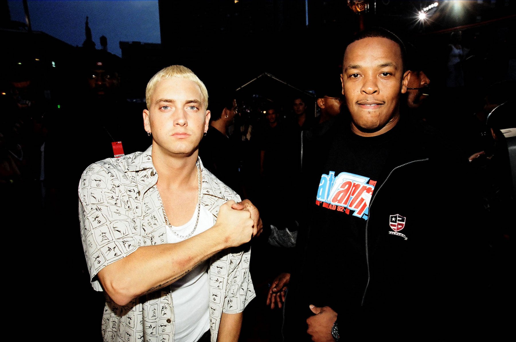 Eminem, wearing white, and Dr. Dre, wearing black, locking hands