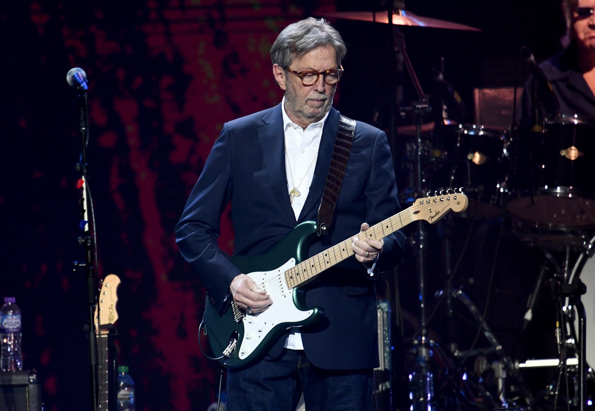 Eric Clapton plays guitar onstage while wearing a blue suit