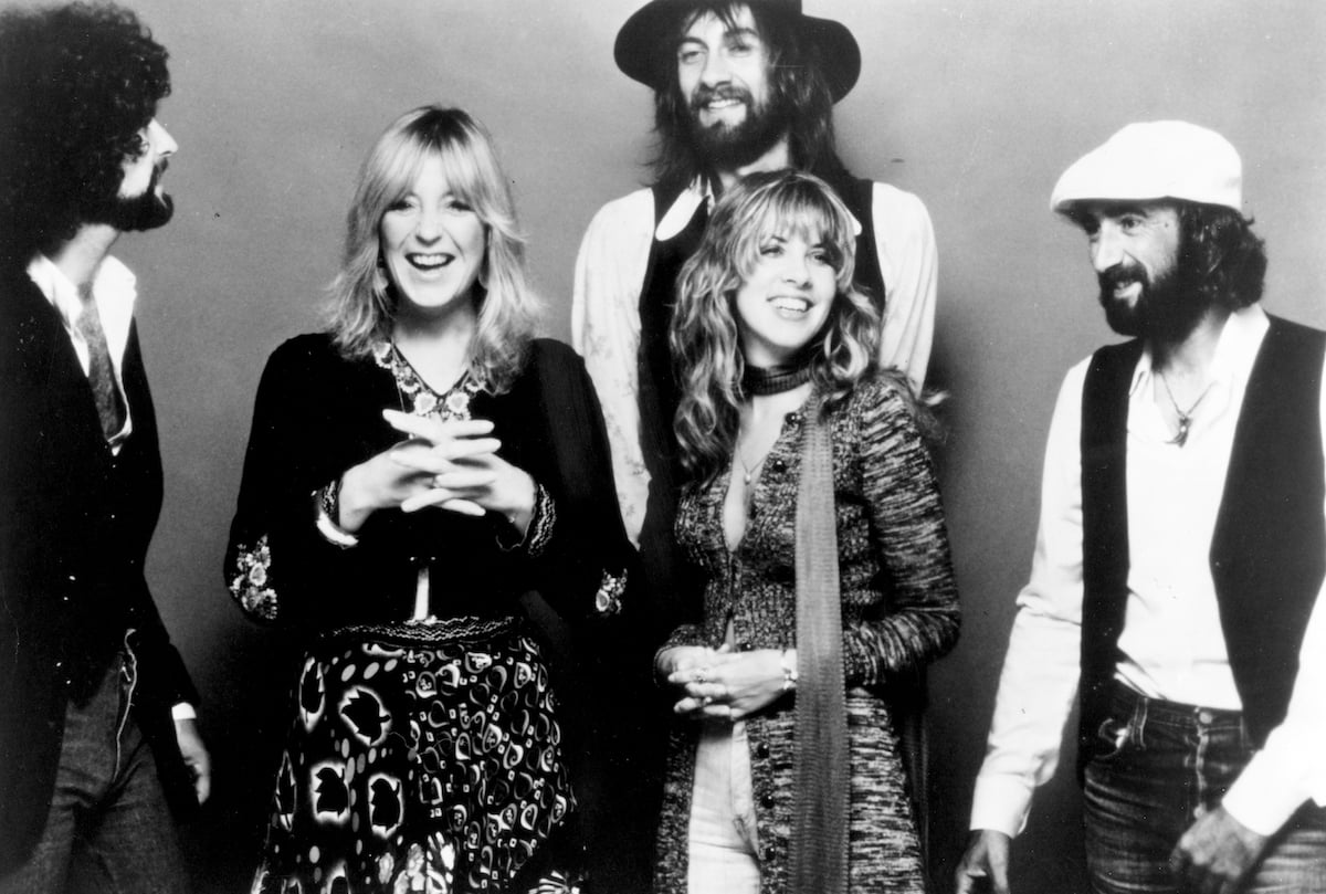 A black and white photo of Fleetwood Mac in their younger years, laughing in a candid shot.