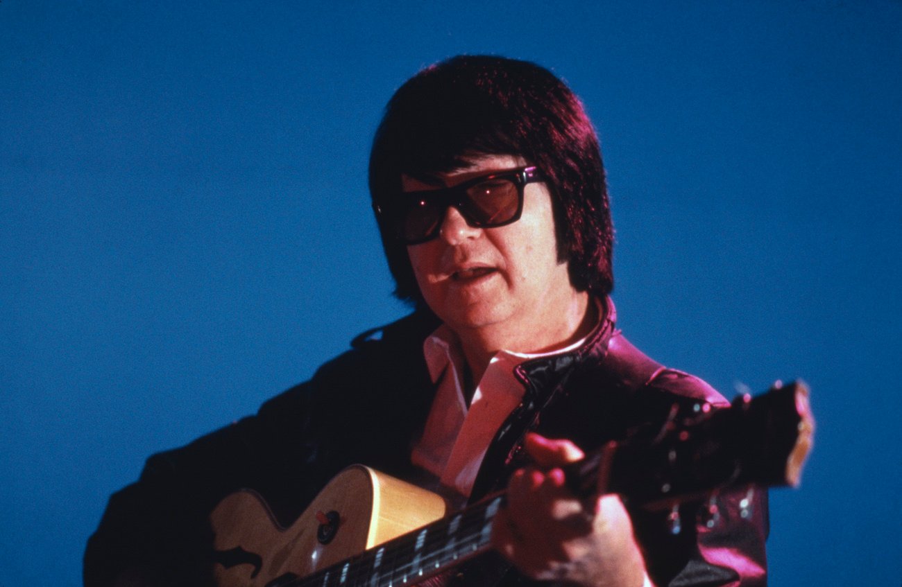 Roy Orbison playing guitar against a blue background in 1980.