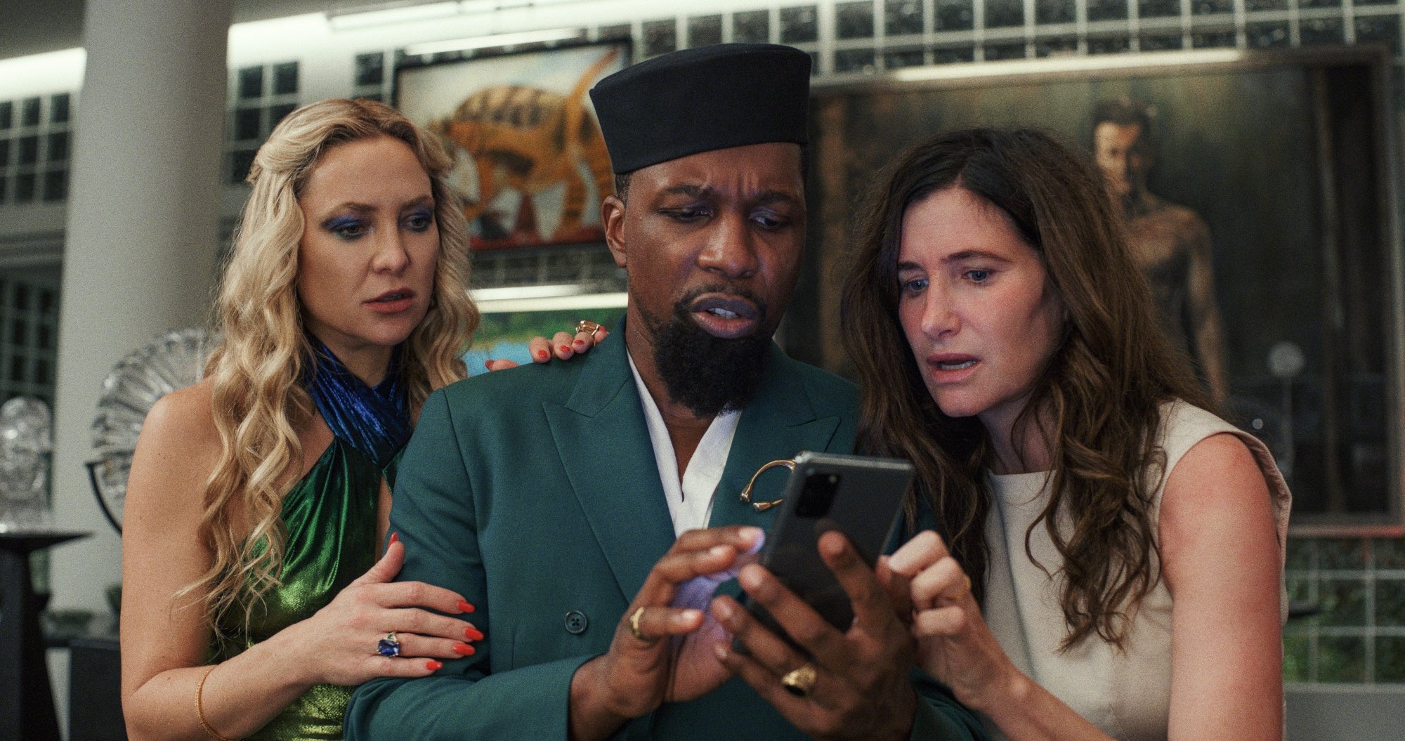 'Glass Onion: A Knives Out Mystery' Kate Hudson as Birdie, Leslie Odom Jr. as Lionel and Kathryn Hahn as Claire looking at the cell phone Lionel is holding in shock.
