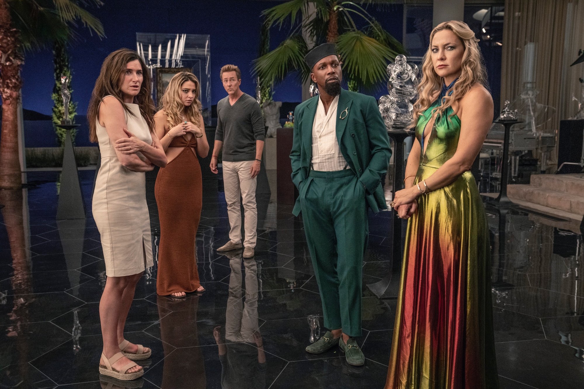 'Glass Onion: A Knives Out Mystery' Kathryn Hahn as Claire, Madelyn Cline as Whiskey, Edward Norton as Miles, Leslie Odom Jr. as Lionel, and Kate Hudson as Birdie all looking shocked standing in a room with black floor and glass statues behind them