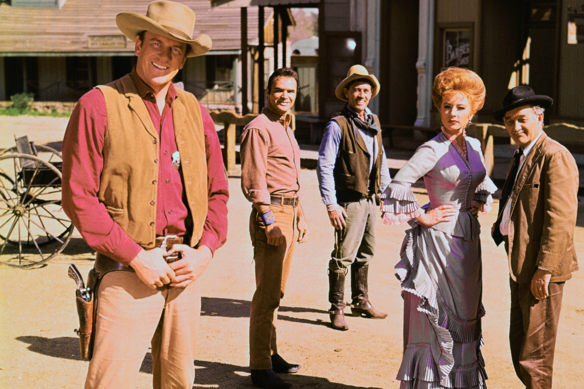 'Gunsmoke' James Arness as Marshal Matt Dillon, Burt Reynolds as Quint Asper, Ken Curtis as Deputy Festus Haggen, Amanda Blake as Kitty Russell and Milburn Stone as Galen Doc Adams standing on a dirt road, looking toward the camera in their character costumes