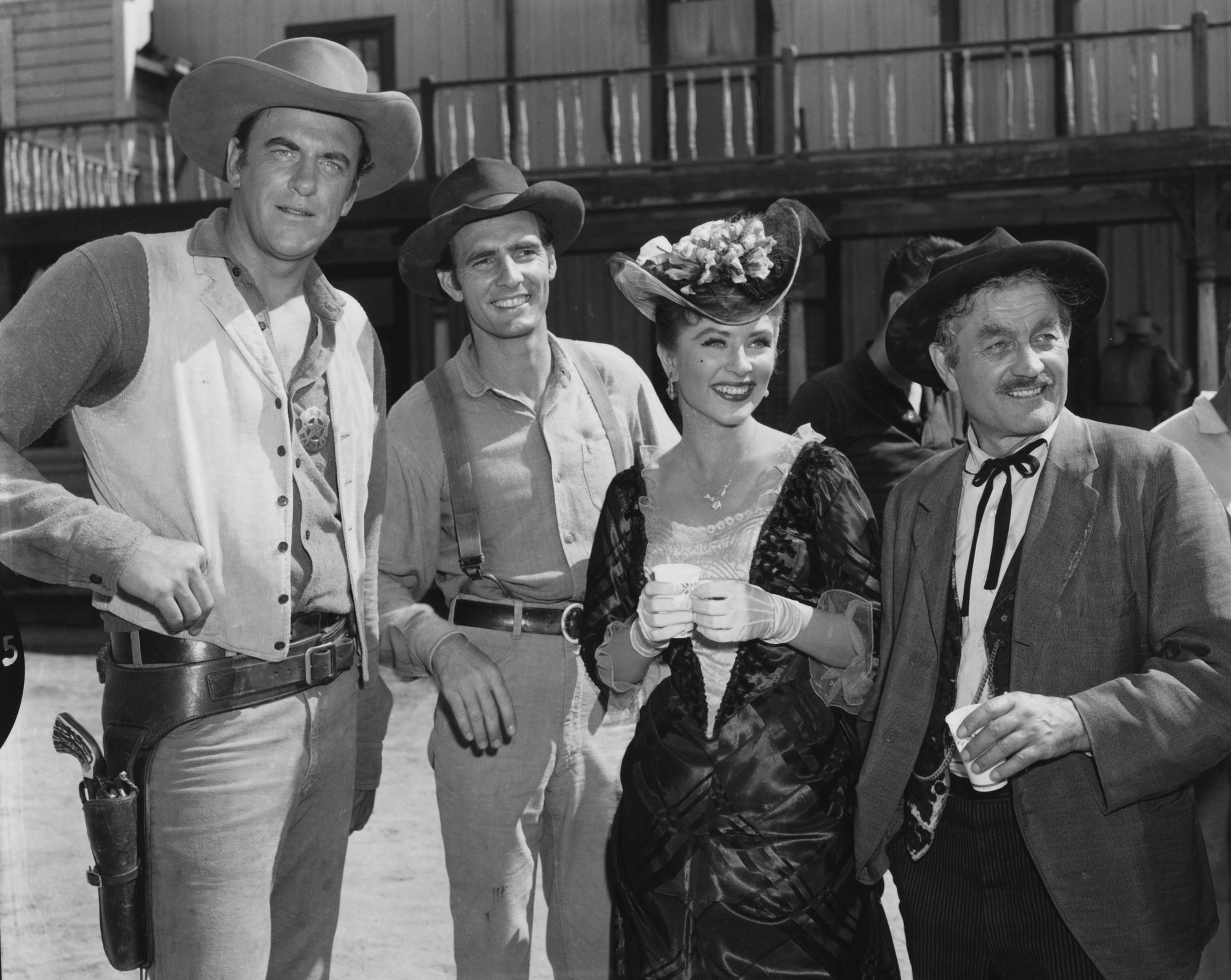'Gunsmoke' James Arness as Marshal Matt Dillon, Dennis Weaver as Chester Goode, Amanda Blake as Kitty Russell, Milburn Stone as Doc Adams in a black-and-white picture, smiling in Western costumes in front of the Dodge City set