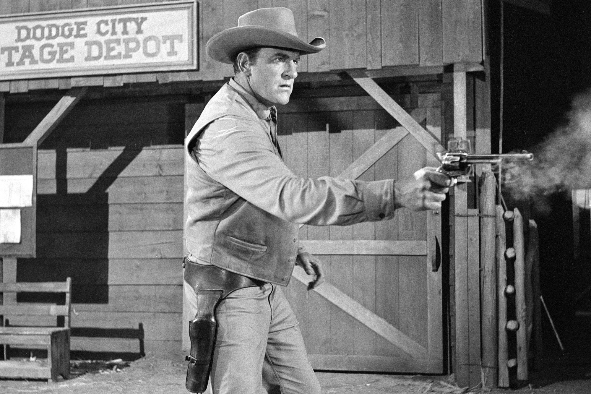 'Gunsmoke' James Arness as Matt Dillon in fight scene. A black-and-white picture with Arness pointing his pistol in front of wooden door.