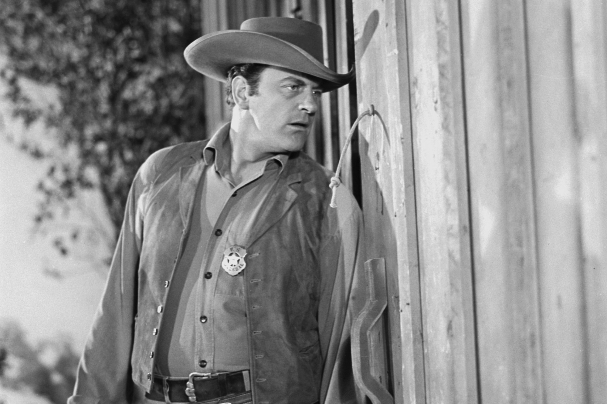 'Gunsmoke' James Arness as Matt Dillon wearing his marshal uniform, lurking behind a wall, spying.