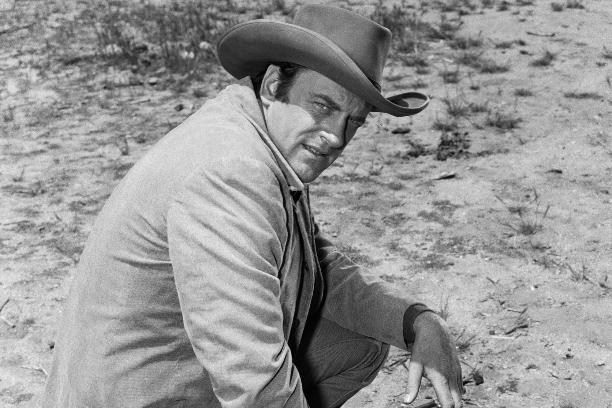 'Gunsmoke' James Arness as U.S. Marshal Matt Dillon kneeling down in the dirt looking over his shoulder