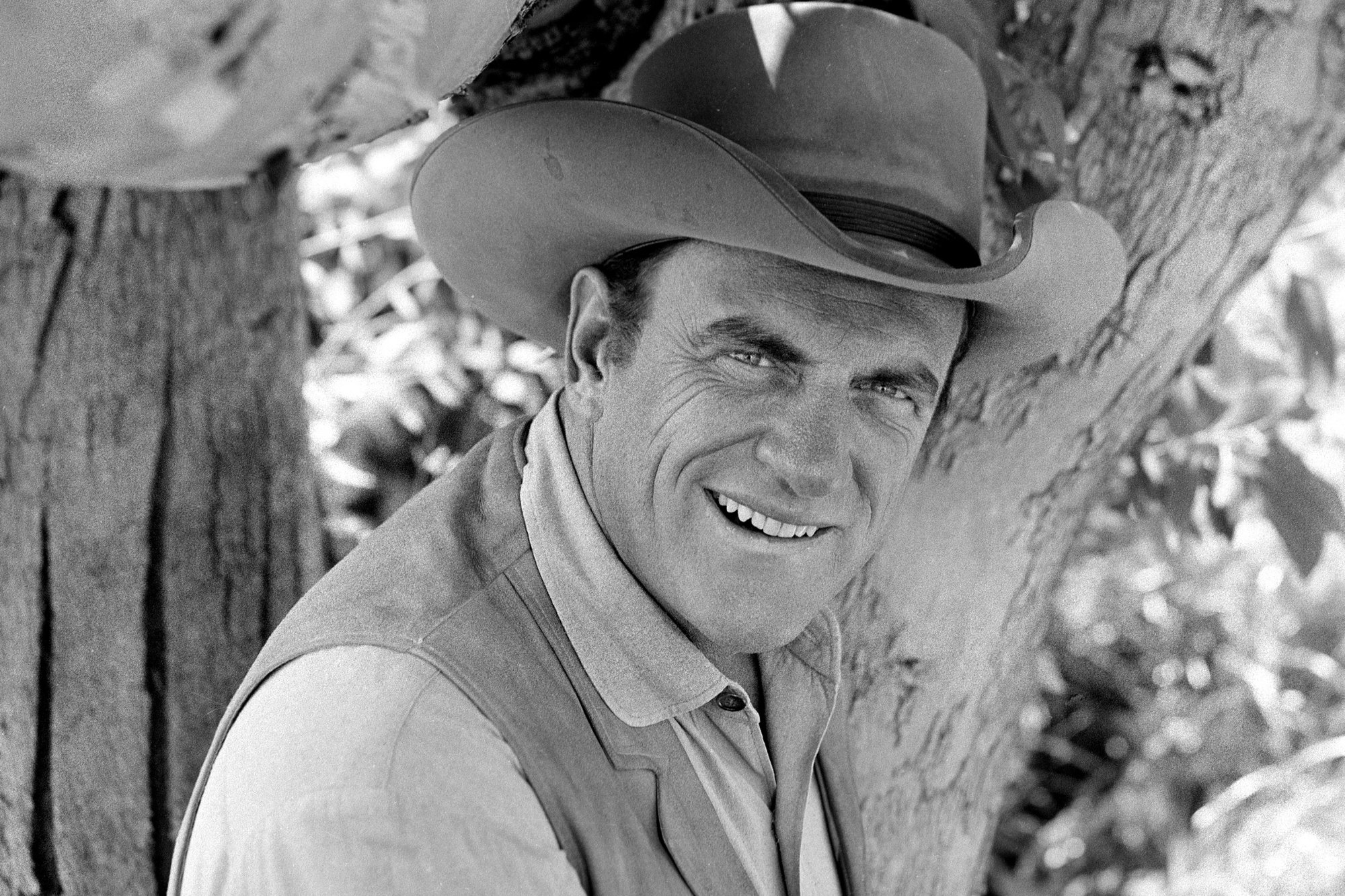 'Gunsmoke' James Arness as U.S. Marshal Matt Dillon, whose death came from natural causes. A black-and-white picture with Arness wearing a cowboy hat, collared shirt, and vest. He's standing in front of a tree.