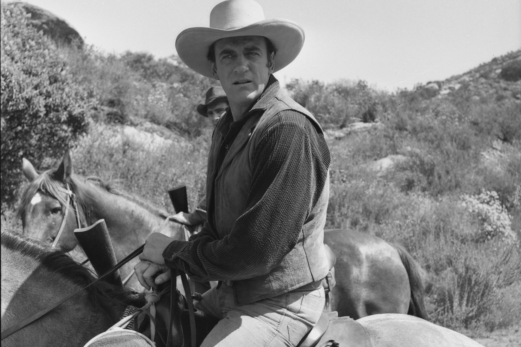 'Gunsmoke' James Arness as U.S. Marshal Matt Dillon in a black-and-white picture on horseback, looking over his shoulder