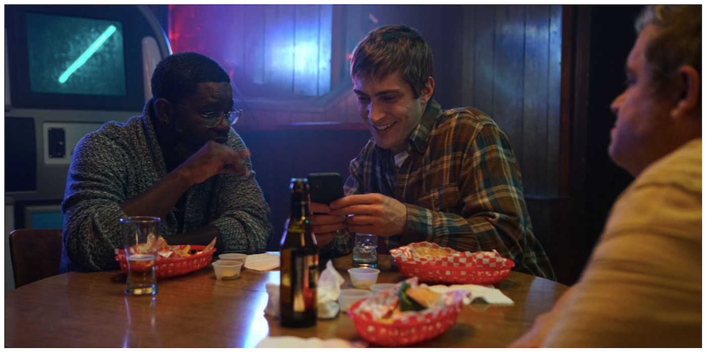 Lil Rel Howery and James Morosini look at a phone and Patton Oswalt looks across the table in 'I Love My Dad.'