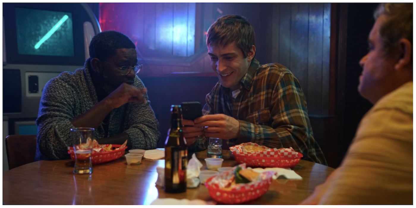 Lil Rel Howery and James Morosini look at a phone and Patton Oswalt looks across the table in 'I Love My Dad.'
