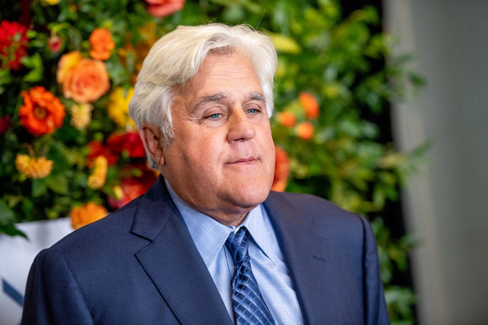 Jay Leno, who was injured in a car fire. He's wearing a navy blue suit and tie with orange and red flowers behind him.