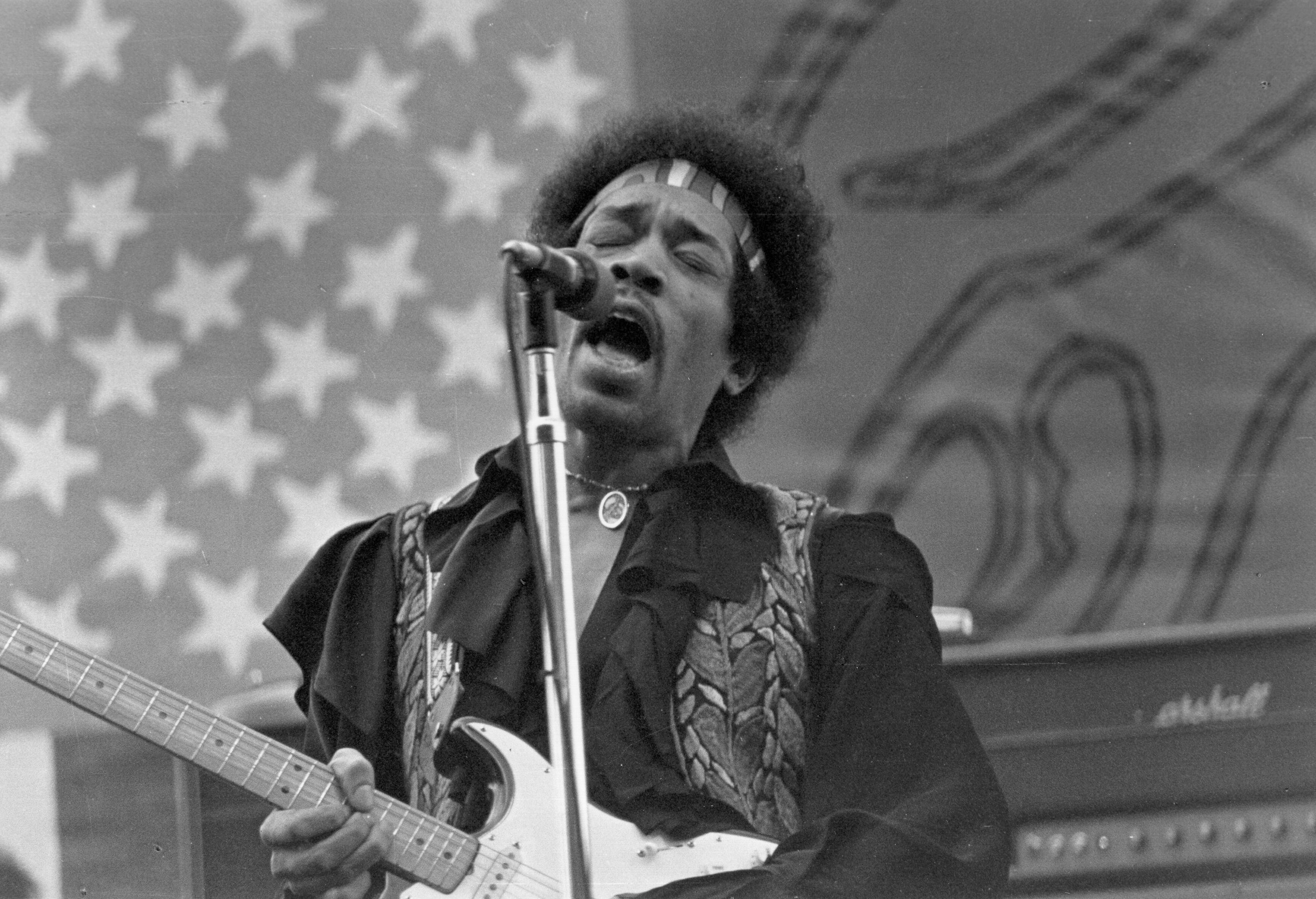 Jimi Hendrix, who formed a band called The Kasuals while in the army, performing in front of an American flag