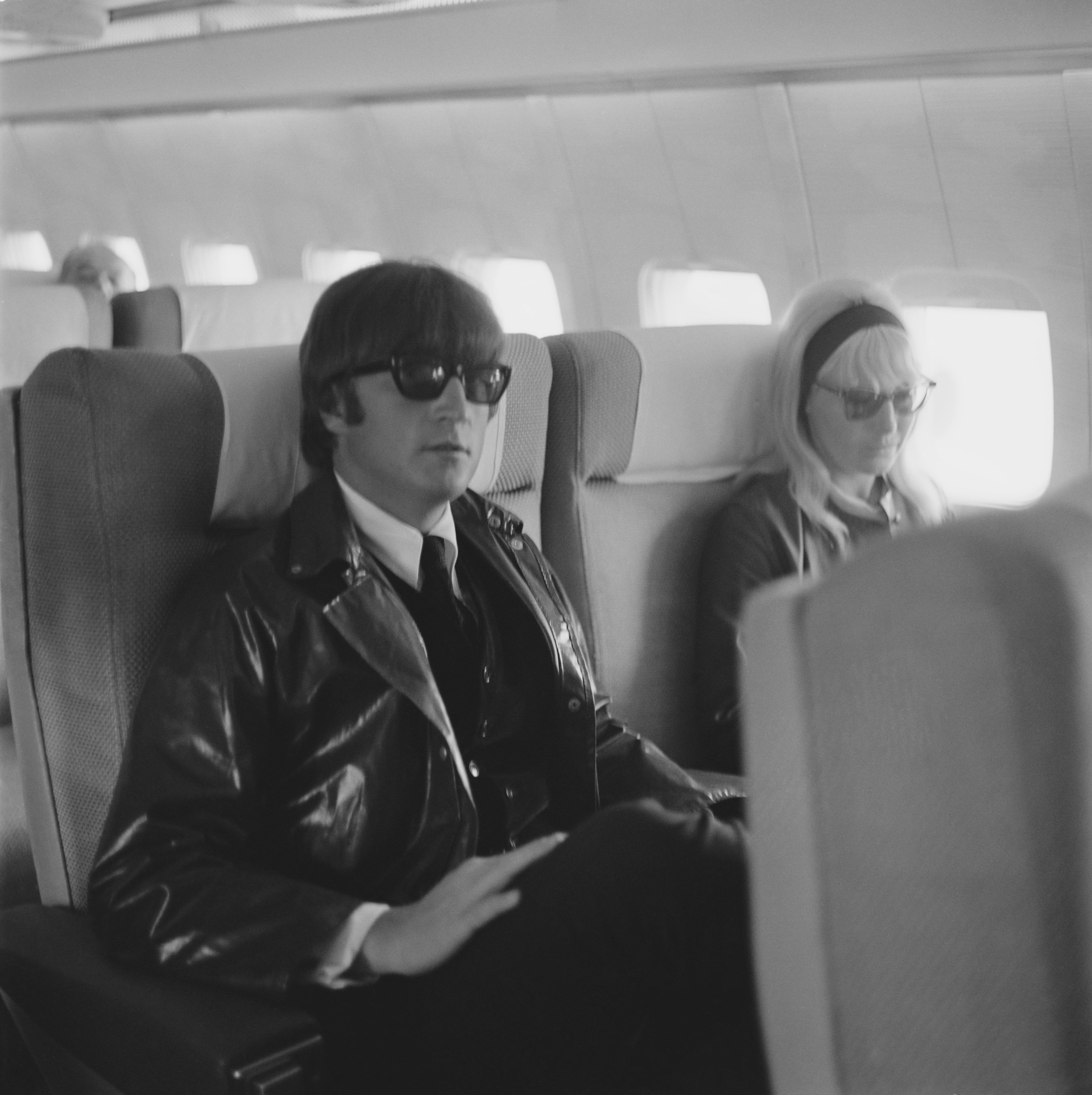 English singer, songwriter, and peace activist John Lennon (1940 - 1980) of the Beatles with his wife Cynthia (1939 - 2015) sitting on an airplane