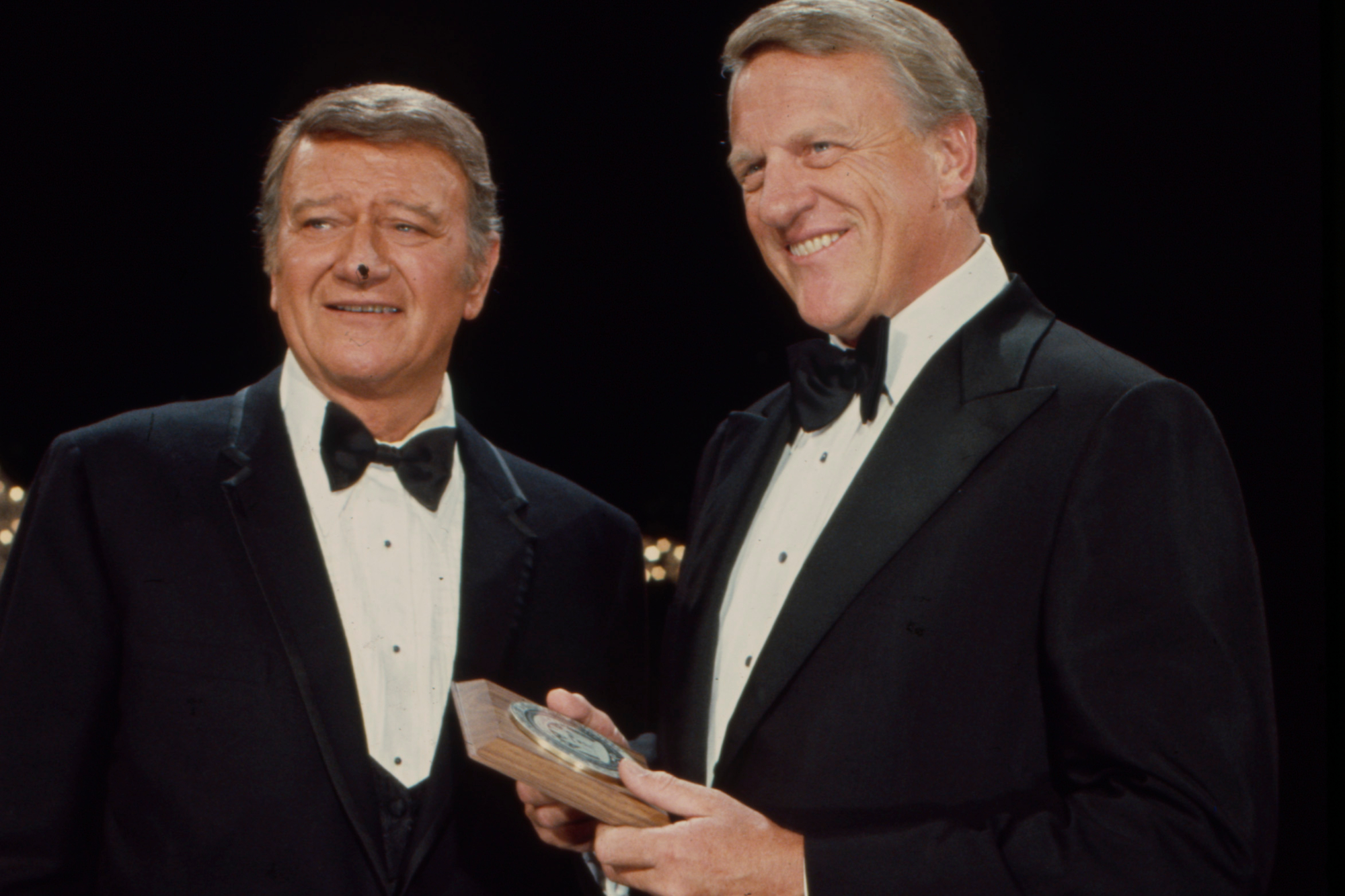 John Wayne and James Arness. They're smiling and wearing tuxes with Arness holding an award.