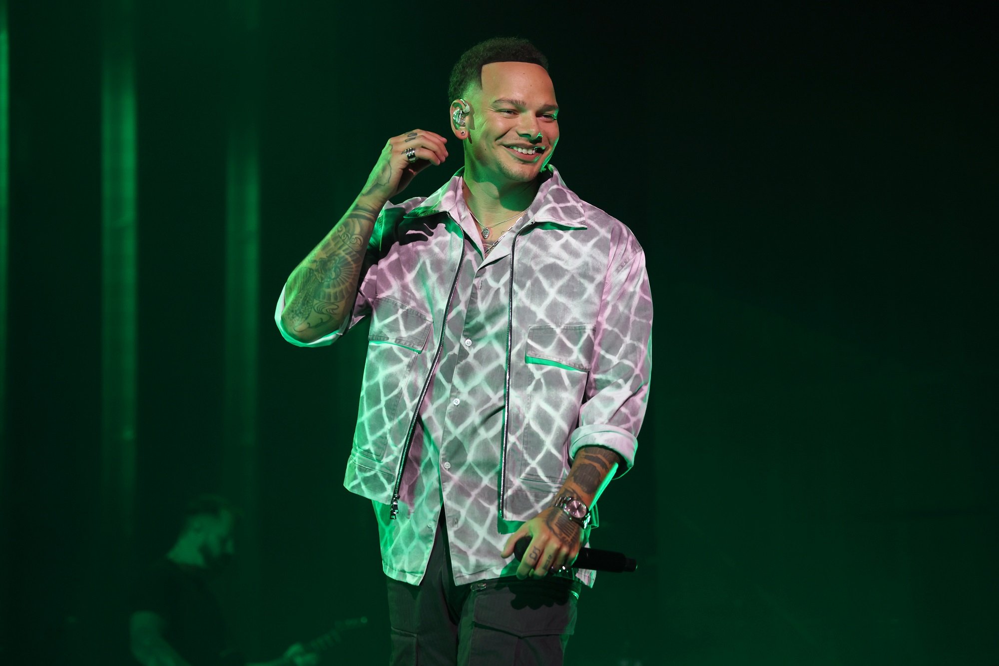 Kane Brown stands on stage with green lighting around him