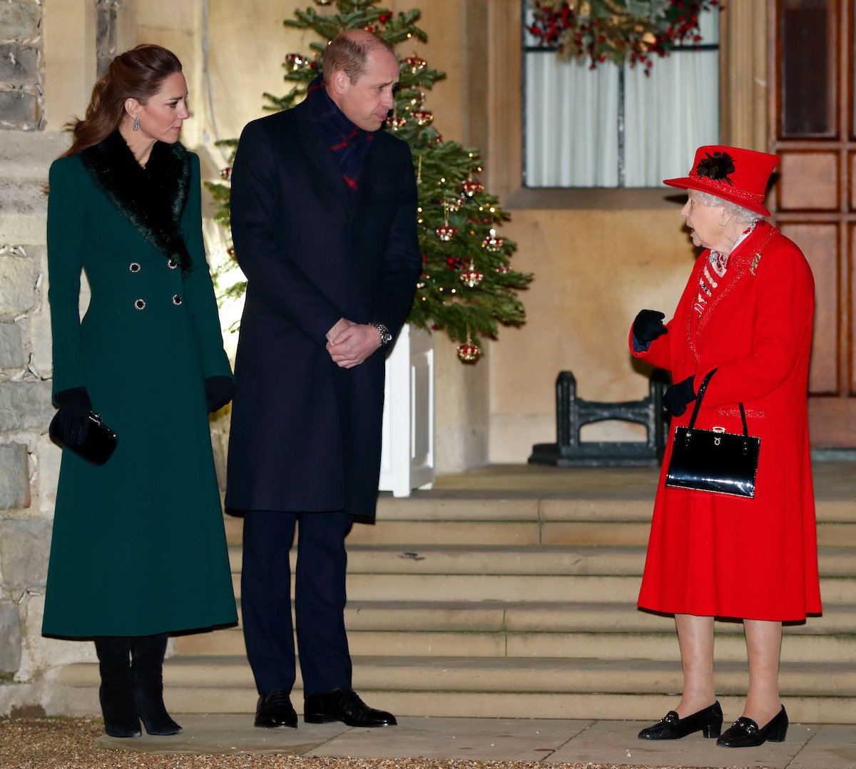 Kate Middleton, whose 2022 Christmas carol concert invitation has a small nod to Queen Elizabeth II, corgis, stands next to Prince William and Queen Elizabeth II in 2020