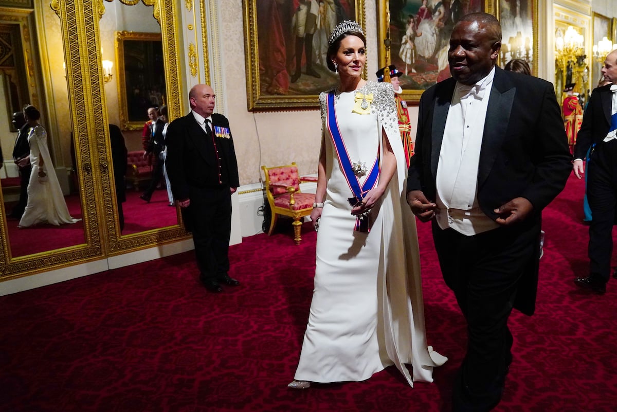 Kate Middleton, wearing a white caped Jenny Packham gown which, according to a commentator, signaled a 'stepping up' in the royal family, walks with guests at Buckingham Palace during a state dinner.