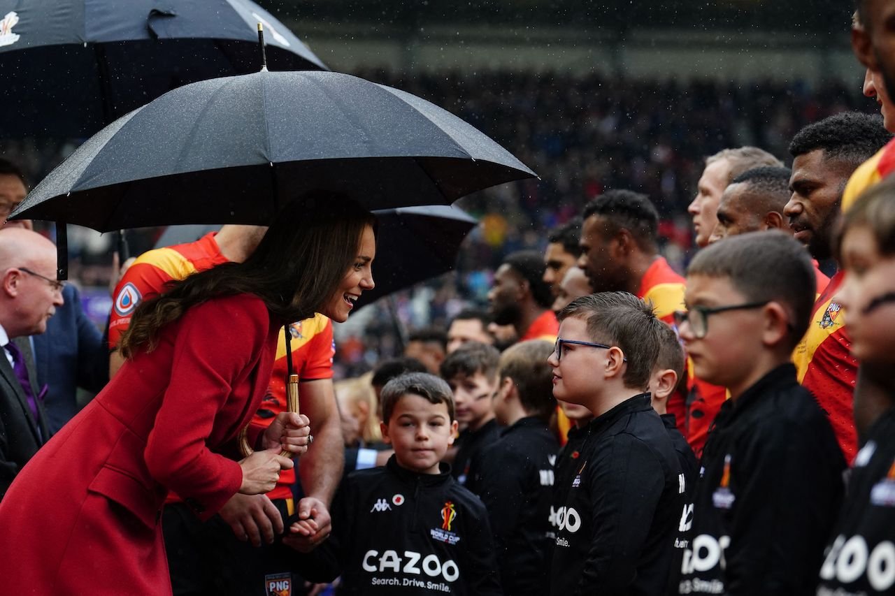 Kate Middleton, Princess of Wales, shelters from the rain under an umbrella as she meets mascots. Royal sources have said her presence in the royal family is "underrated."