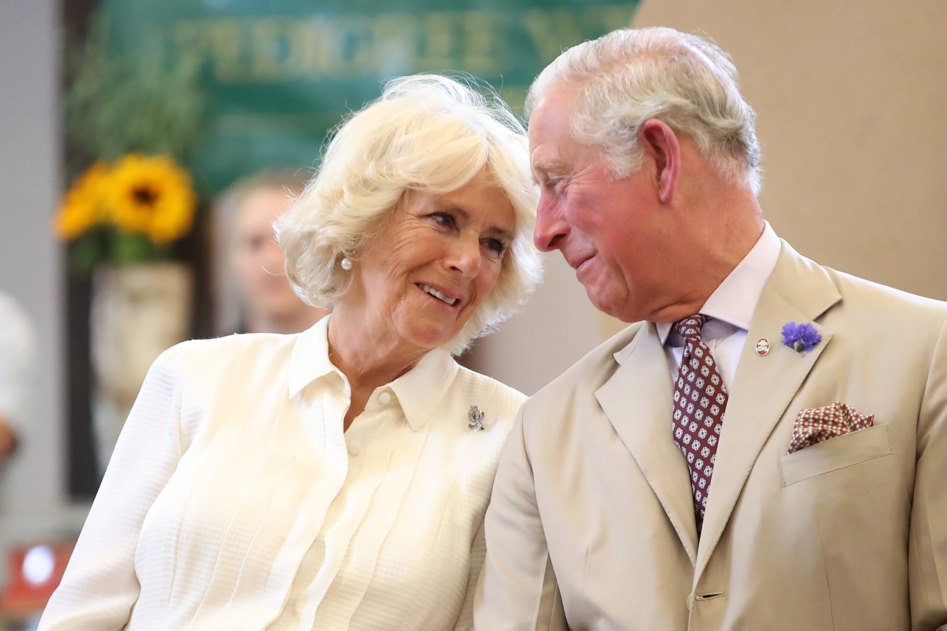 Queen Camilla and King Charles sit next to each other and smile.