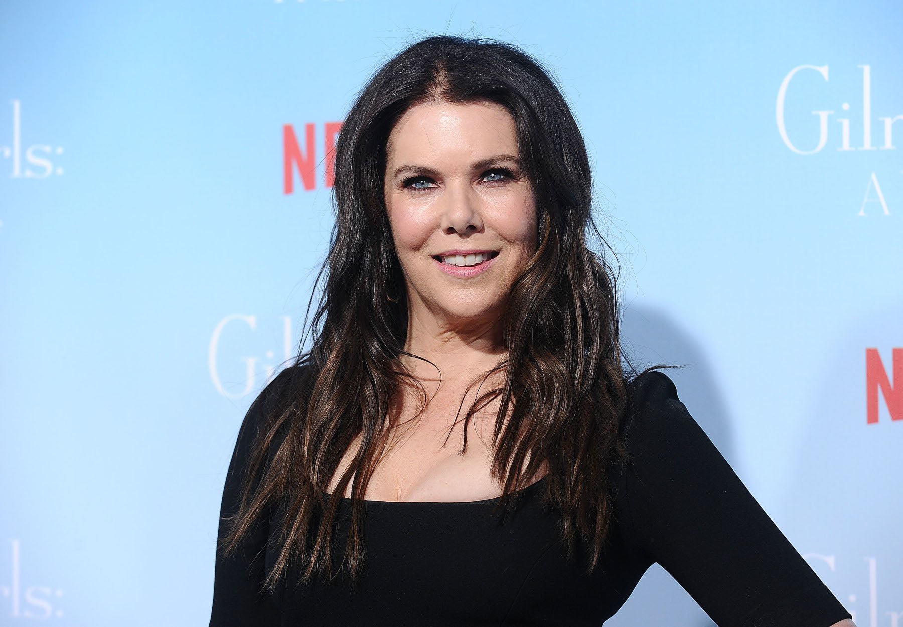 'Gilmore Girls' star Lauren Graham, who commented on an alternate title for the show. She's standing in front of a blue wall with the Netflix logo. Her shirt is black, and her hair is curled.