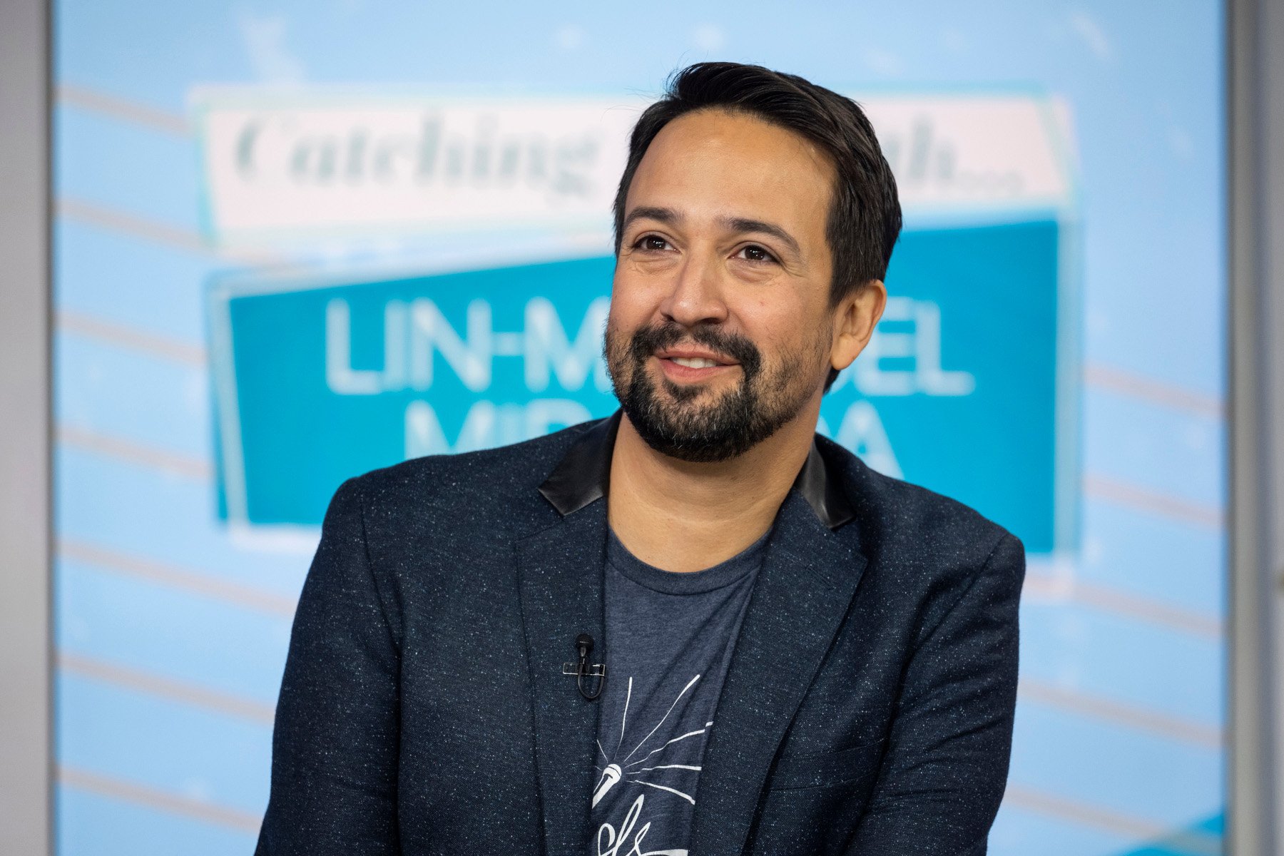 Lin-Manuel Miranda for our article about the 'Percy Jackson and the Olympians' cast. He's wearing a dark blue T-shirt, blue blazer, and smiling.