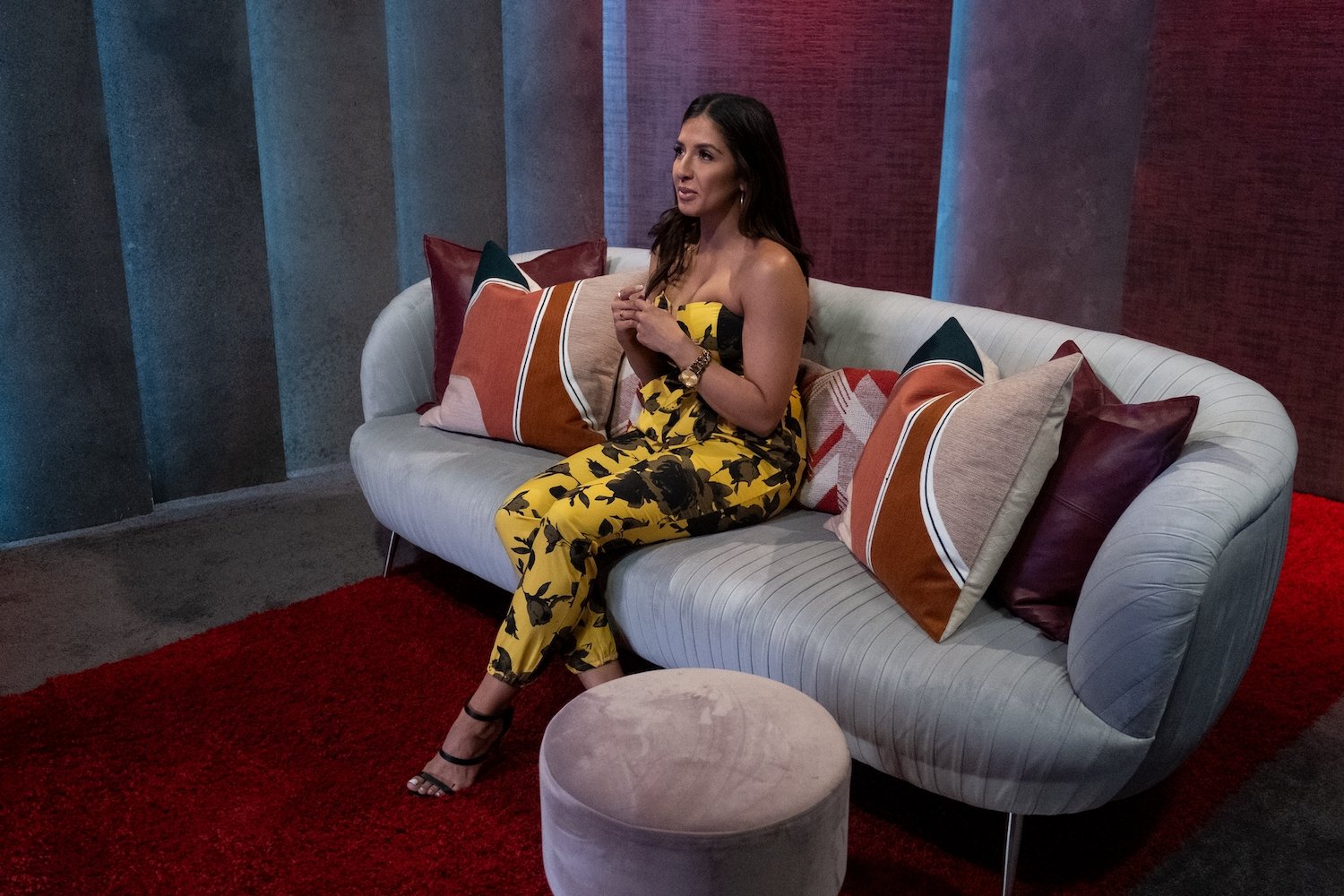 'Love Is Blind' star Zanab Jaffrey sitting on a couch in the pods wearing a yellow jumpsuit.