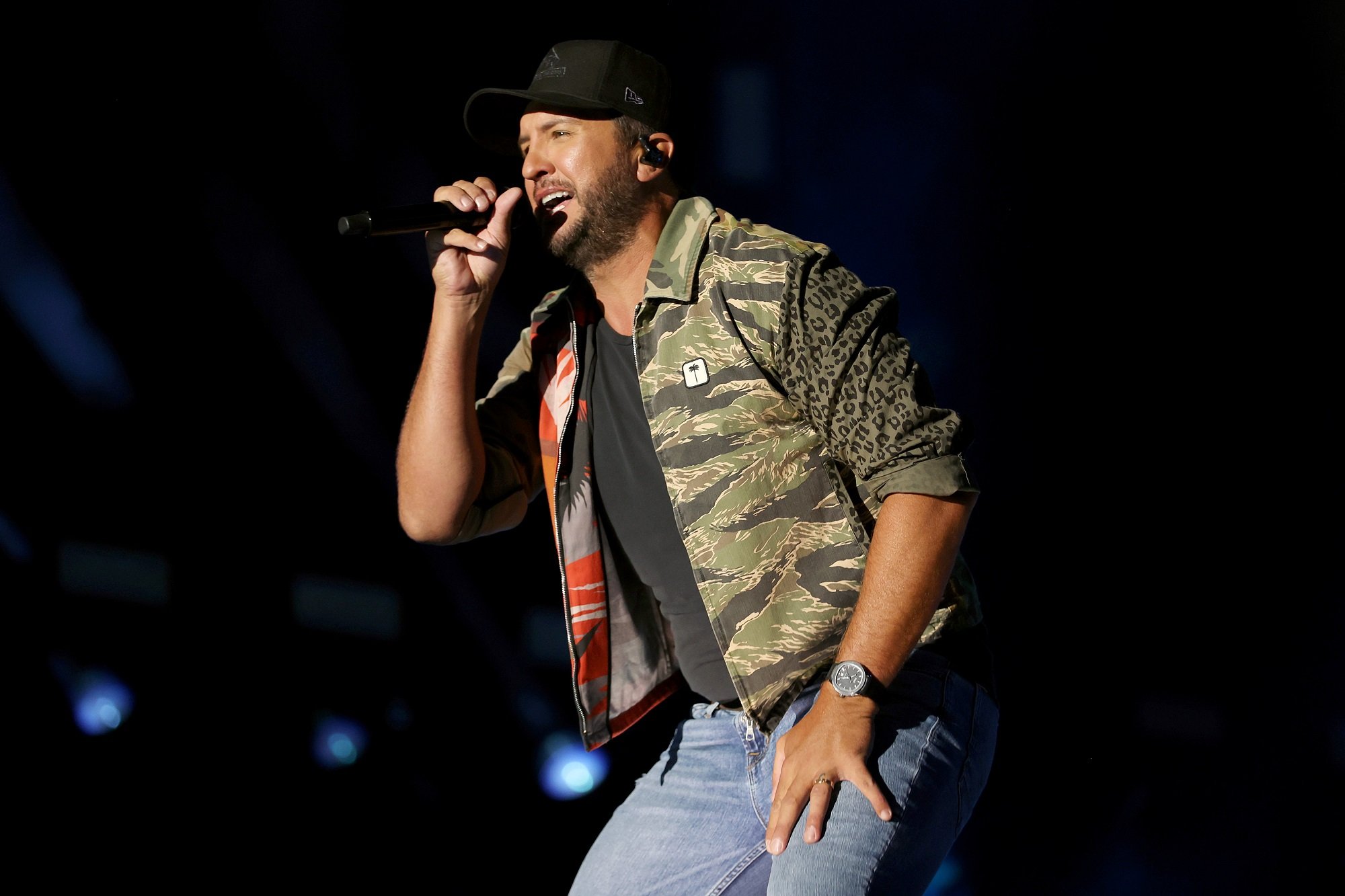 Luke Bryan performs wearing a black baseball cap, a green jacket, and jeans