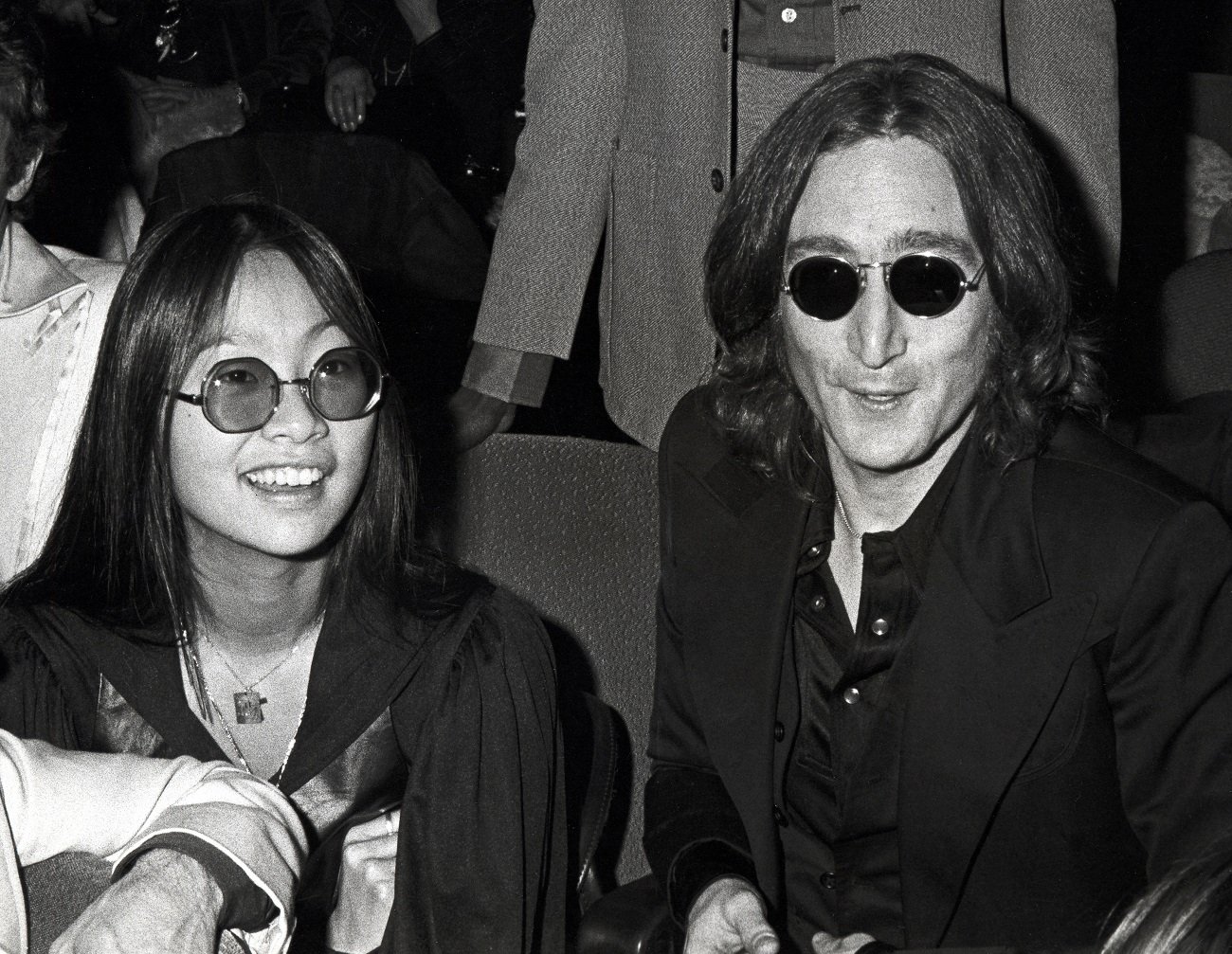 May Pang and John Lennon sit together and both wear sunglasses.