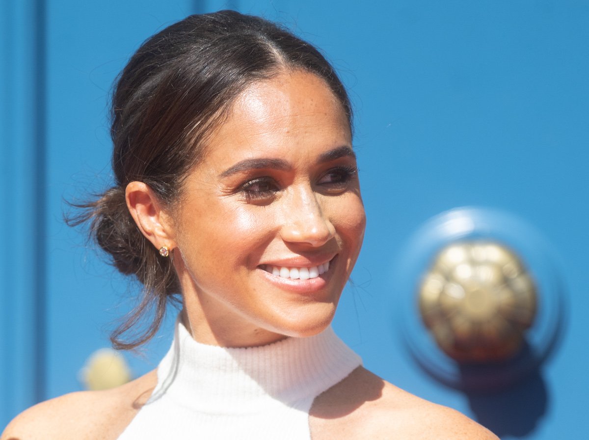 Meghan Markle smiles in a white high collar top