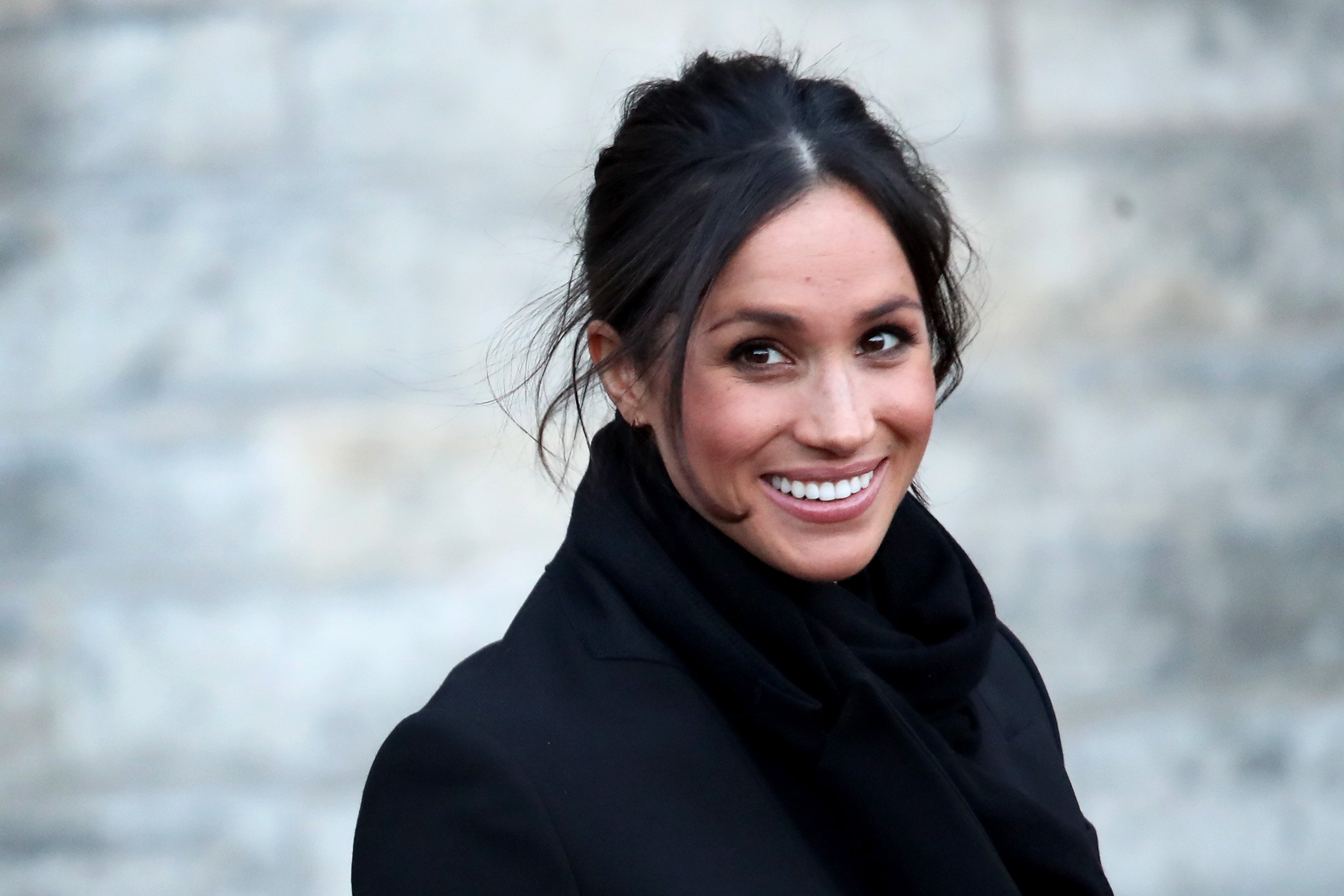 Meghan Markle smiles while wearing a black outfit.