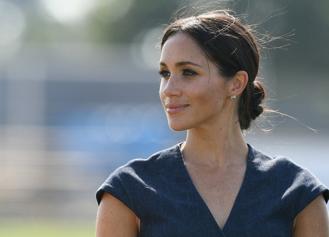 Meghan Markle stands outside and smiles. 