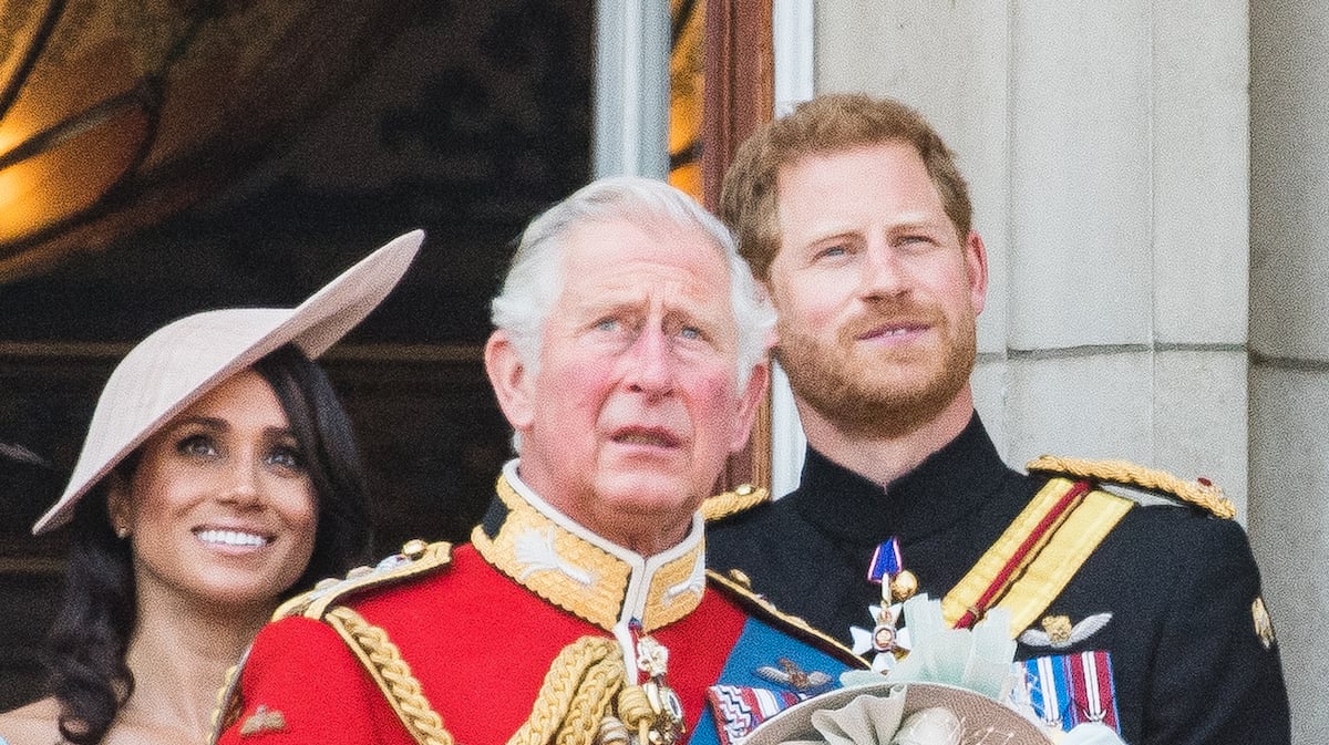Meghan Markle and Prince Harry, whose invite to King Charles III's coronation 'depends' on the 'next few months' according to podcast hosts, stand behind King Charles 