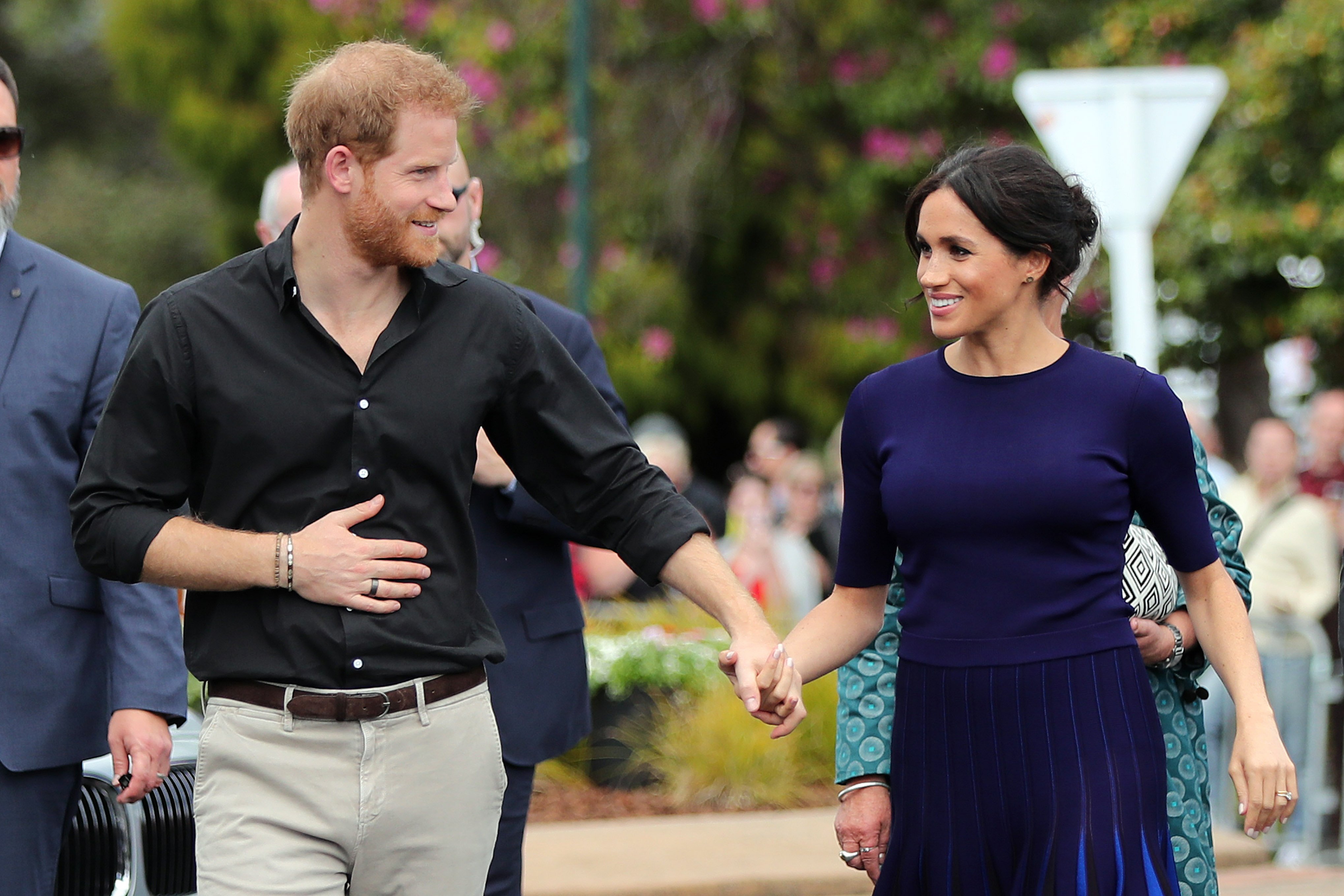 Prince Harry and Meghan Markle hold hands as they walk.