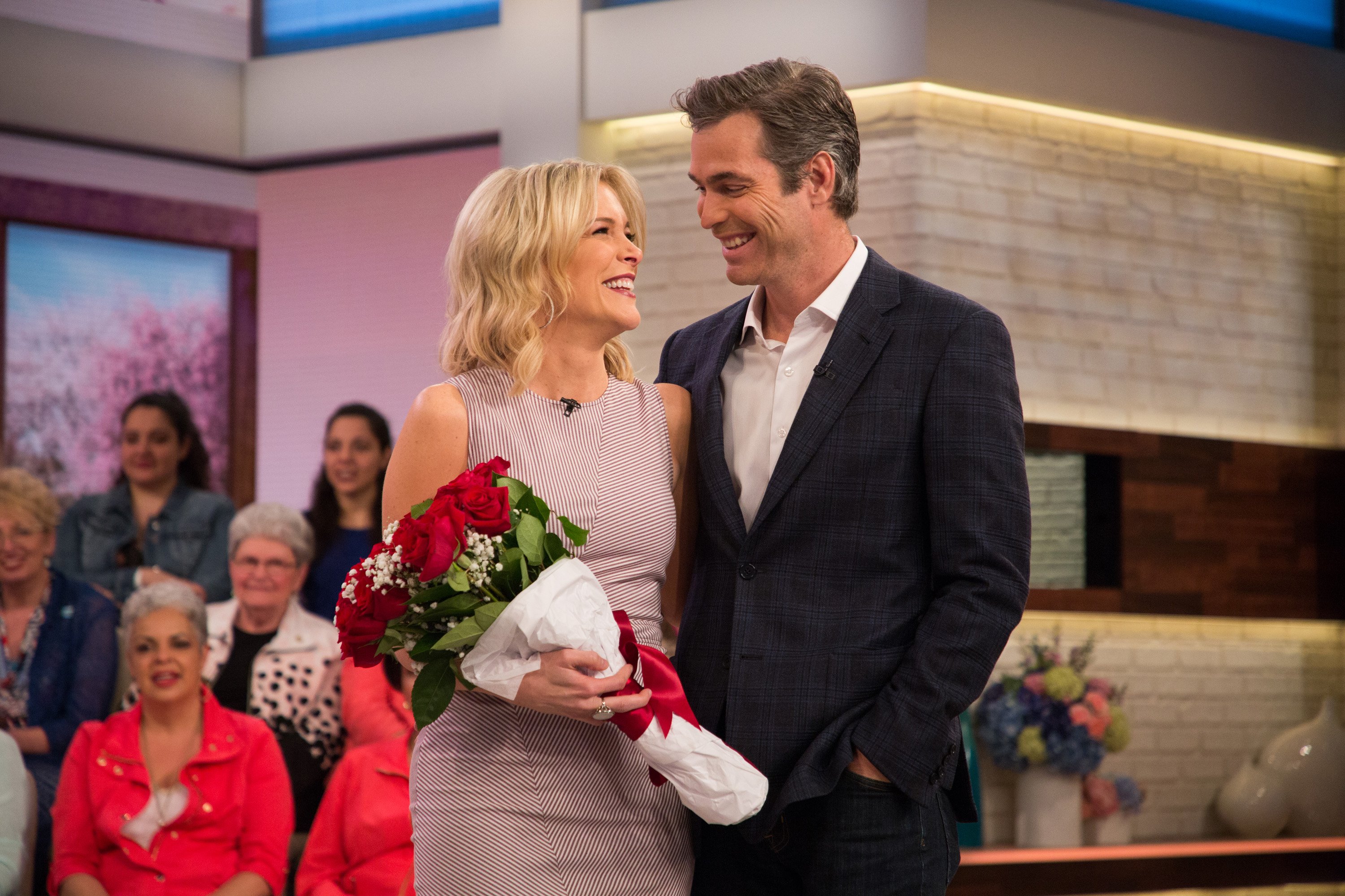 Megyn Kelly and Doug Brunt stand next to each other while she holds a bouquet of flowers and smiles.