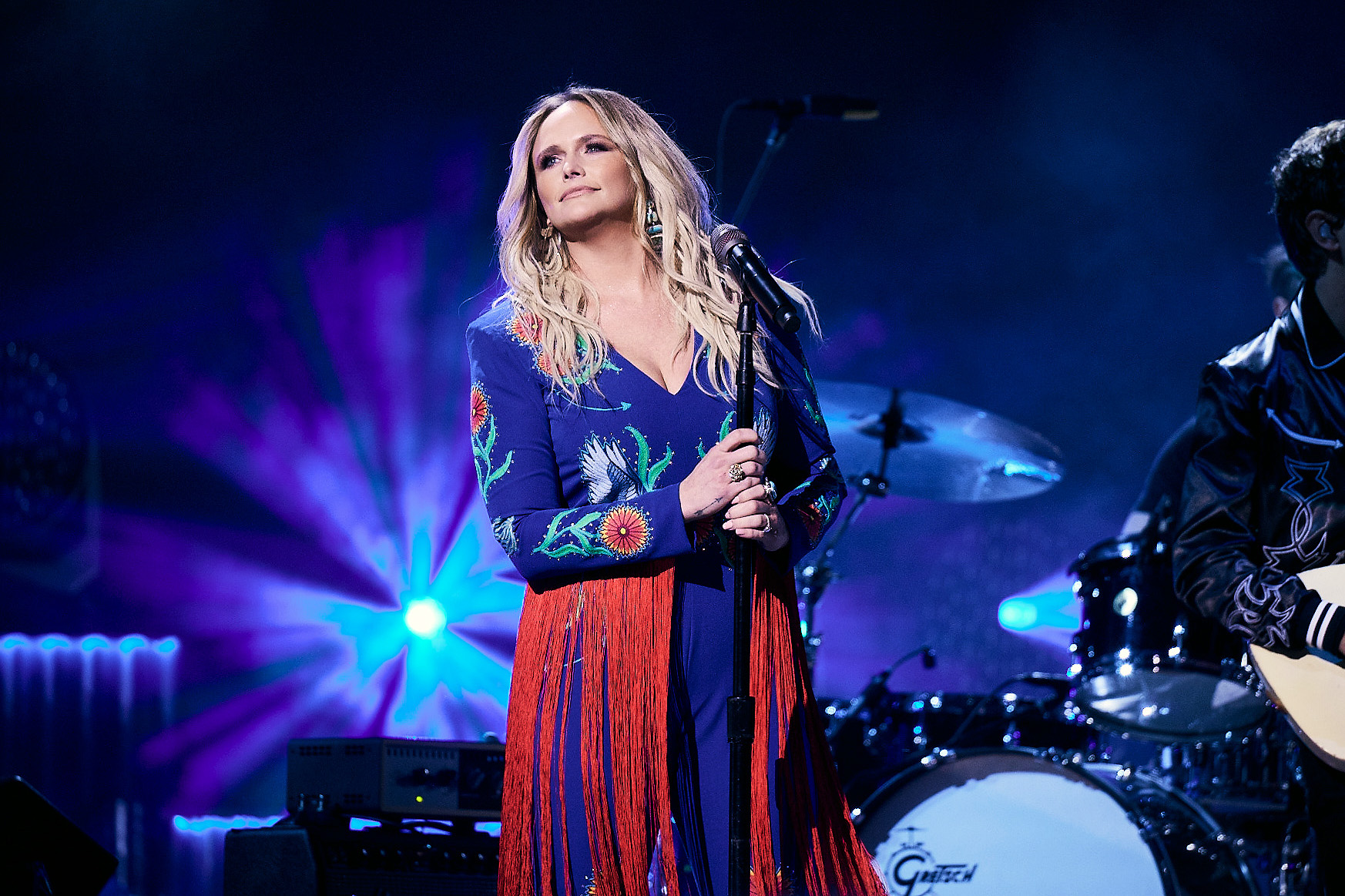 Miranda Lambert wears a red and blue outfit on stage and holds a microphone stand