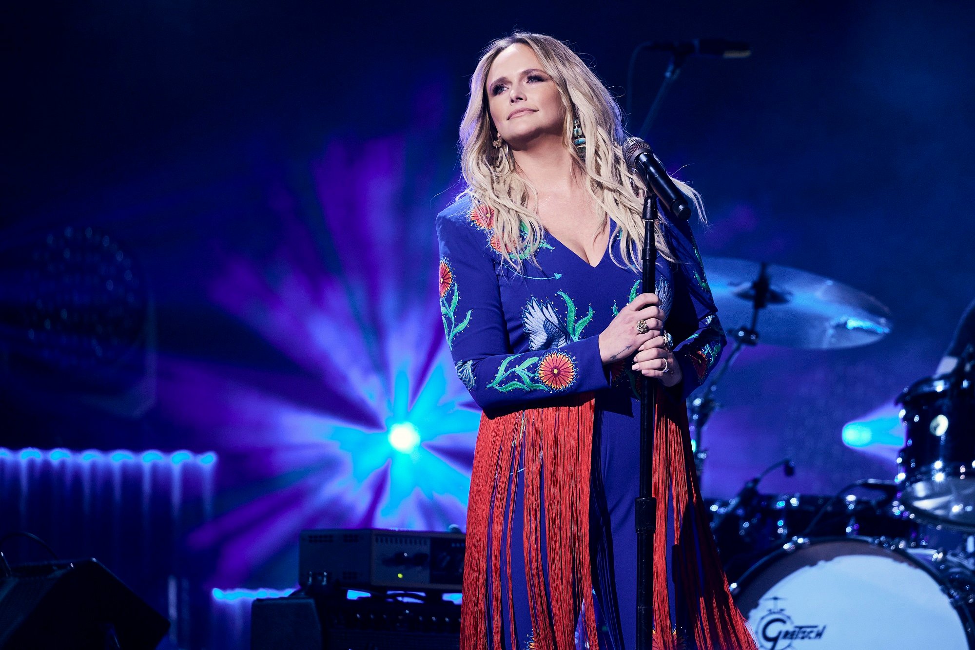 Miranda Lambert holds a microphone stand while wearing a blue-and-red outfit