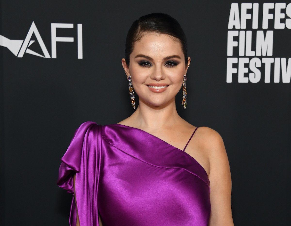 My Mind & Me star Selena Gomez smiles at the camera in a purple dress and dangling earrings