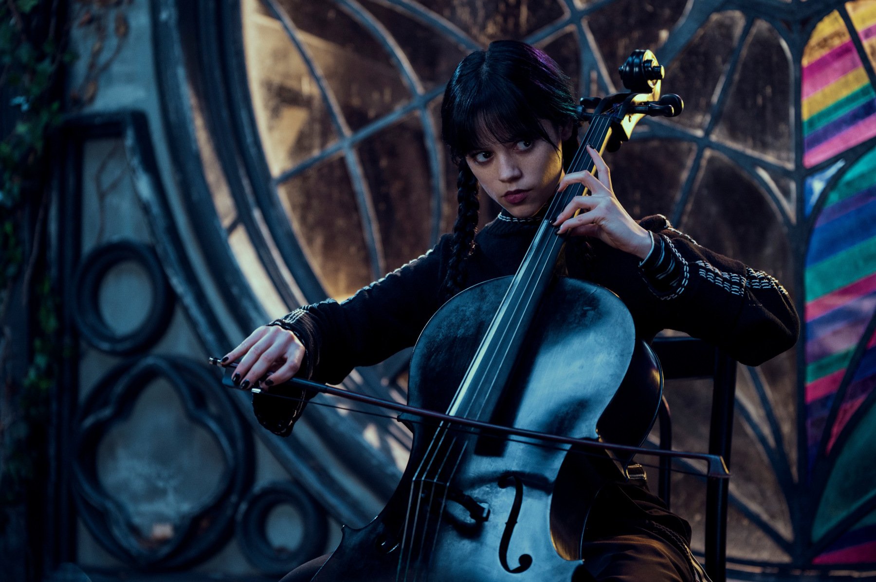 Jenna Ortega in 'Wednesday' for our list of new shows and movies coming out on Netflix this week. Her black hair is in braided pigtails, and she's playing the violin.