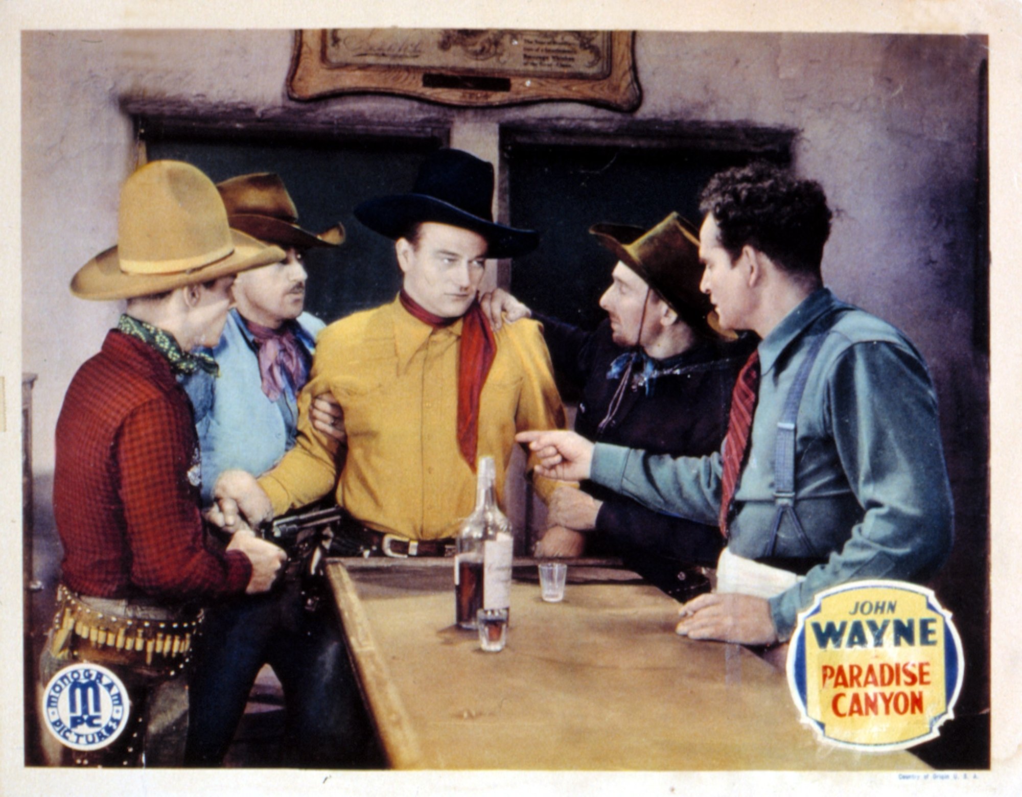 'Paradise Canyon' John Wayne and actor, stunt double Yakima Canutt. They're standing around a table wearing Western clothing looking tense.