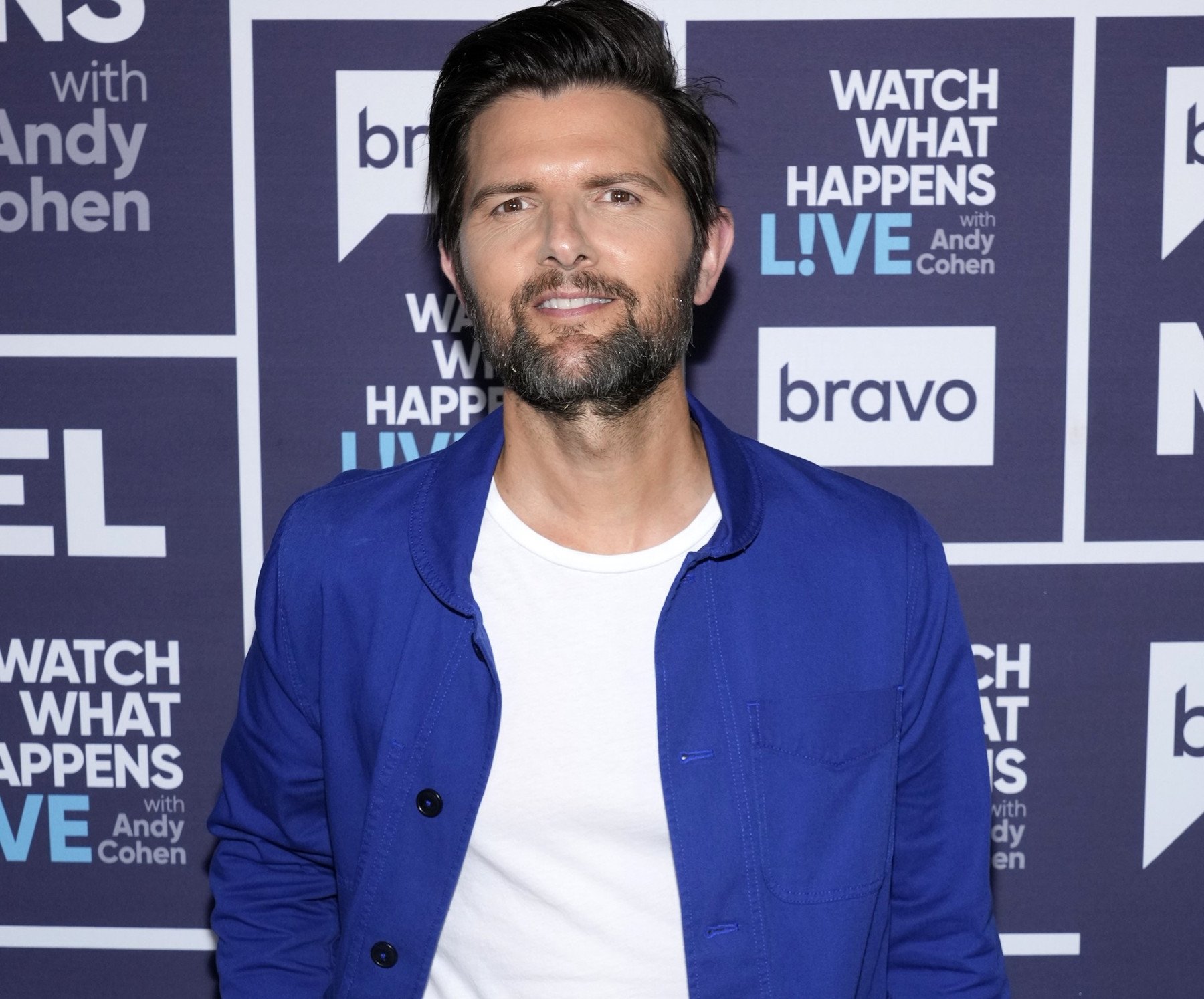 'Parks and Rec' cast member Adam Scott. He's wearing a white T-shirt and blue jacket and standing in front of a Bravo wall.