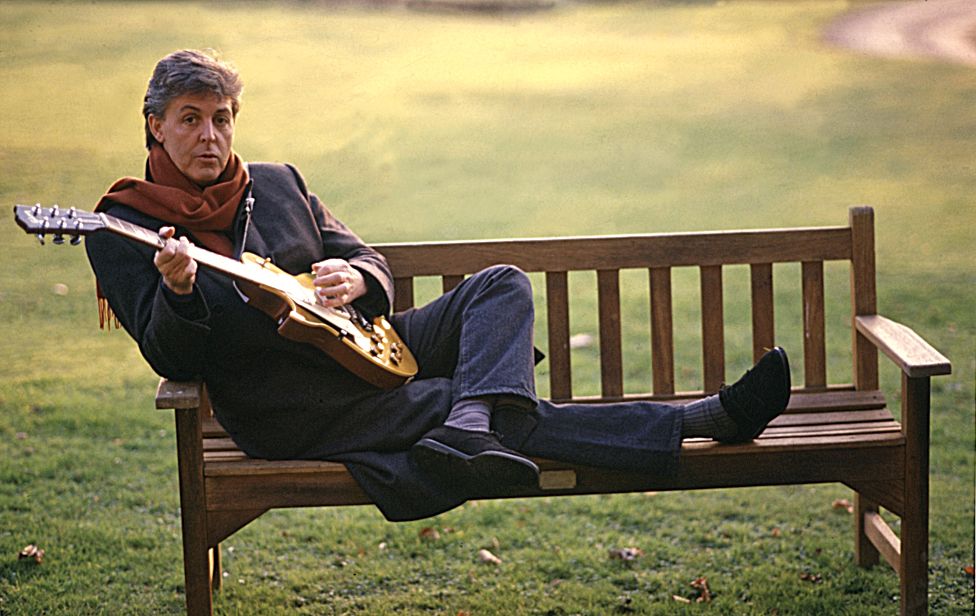 Paul McCartney poses on a bench while playing guitar in 1987