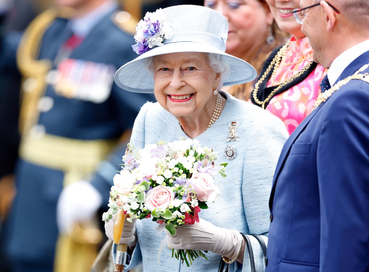 Queen Elizabeth II, who refused to hold a sword in her 2002 Golden Jubilee portrait because she didn't like her hands, according to photographer Rankin, smiles wearing gloves and holding flowers in 2022