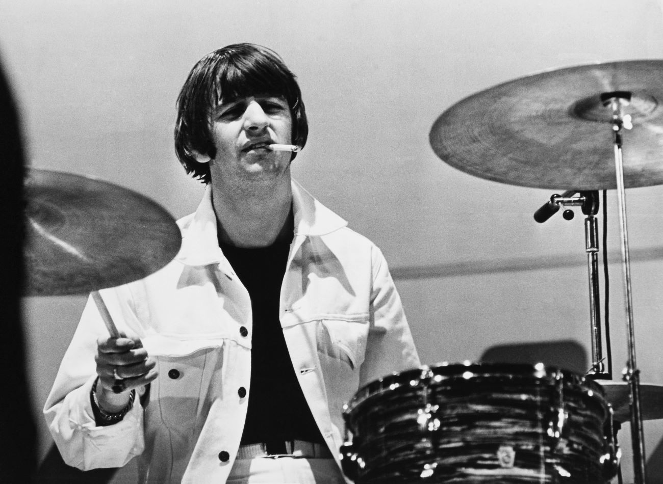 A black and white picture of Ringo Starr drumming with a cigarette in his mouth.