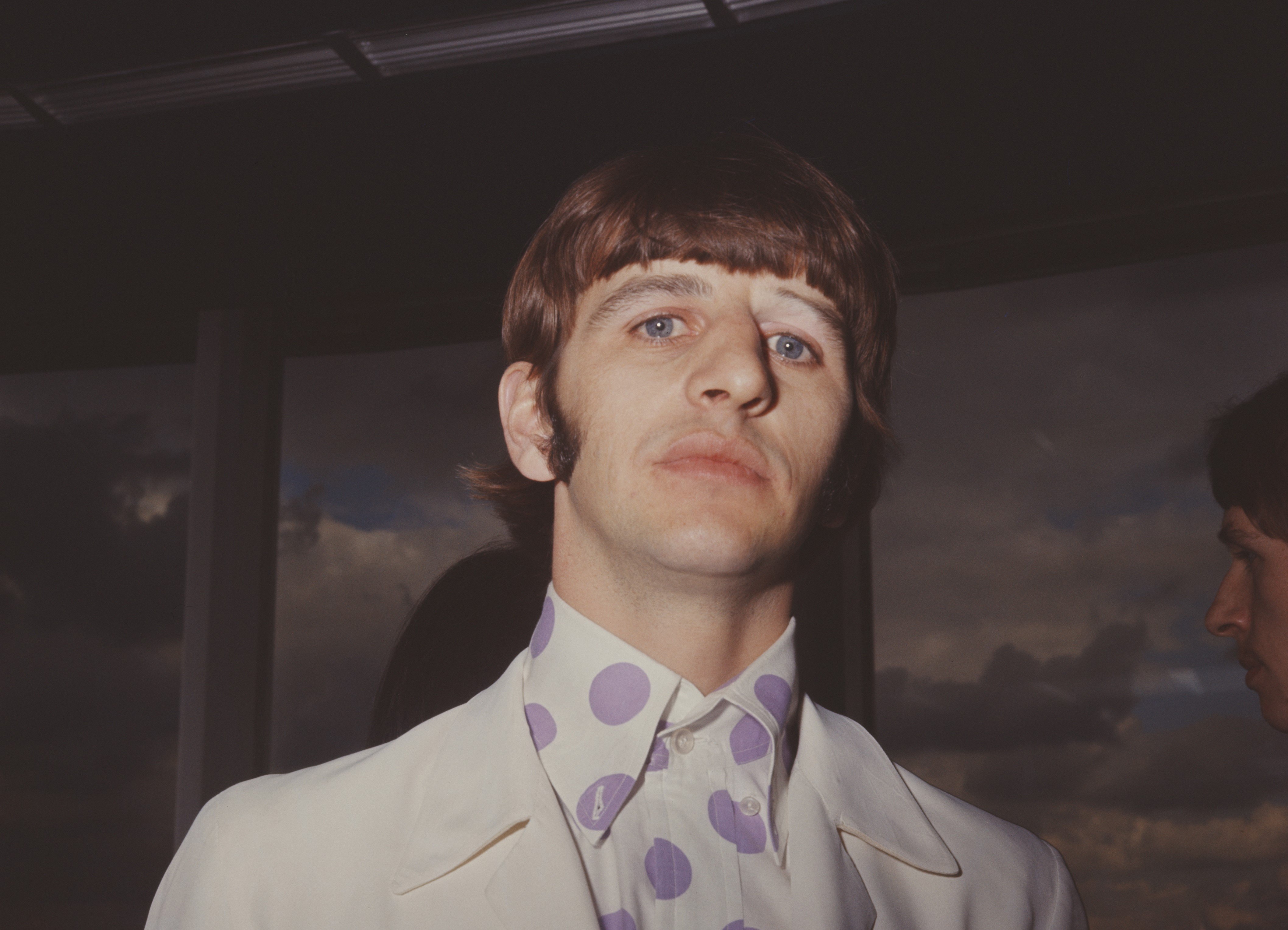 Ringo Starr wears a polka dotted shirt and a white jacket.