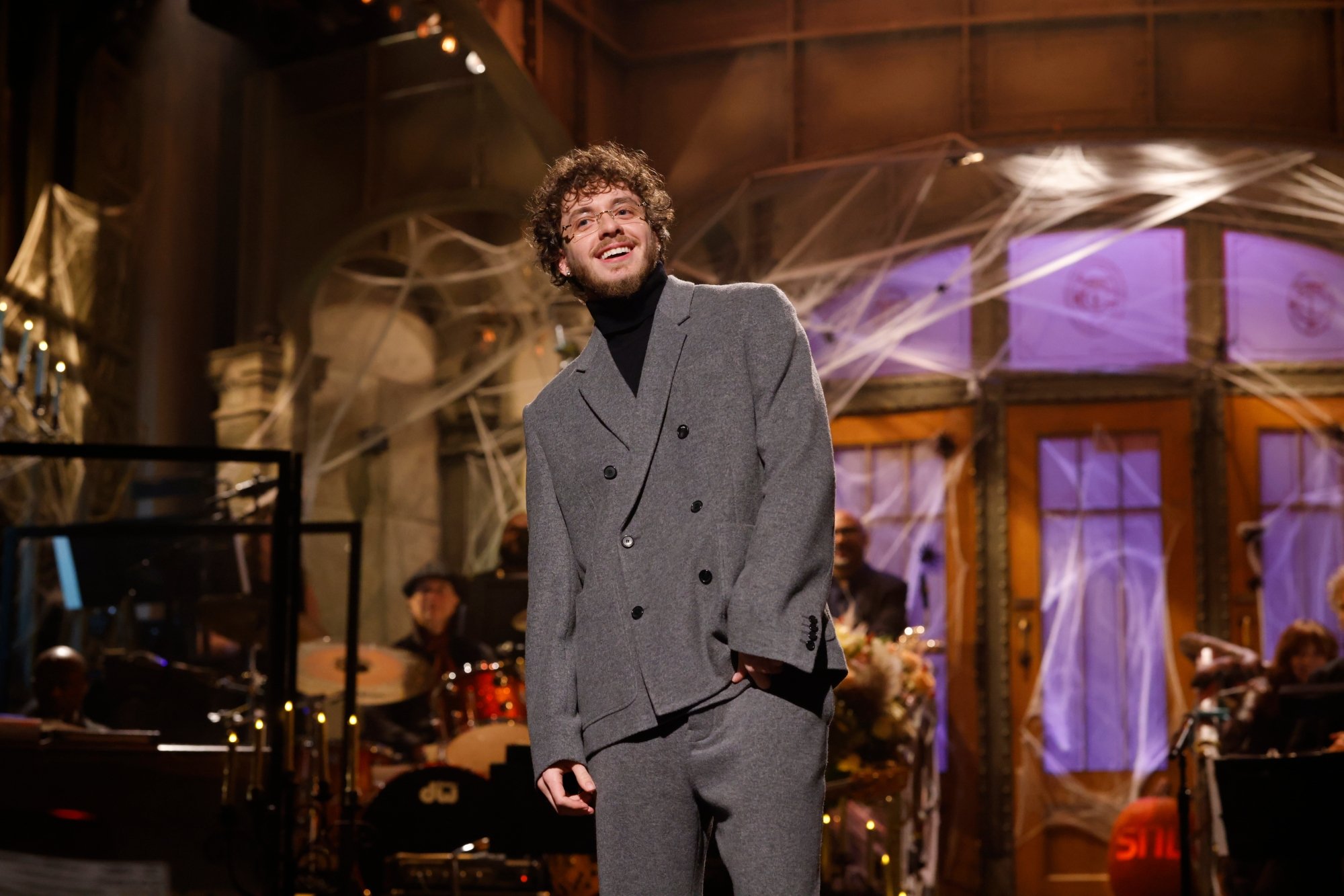 'Saturday Night Live' host Jack Harlow on horror episode. Harlow is smiling in a baggy suit jacket and pants in front of Halloween-themed set.