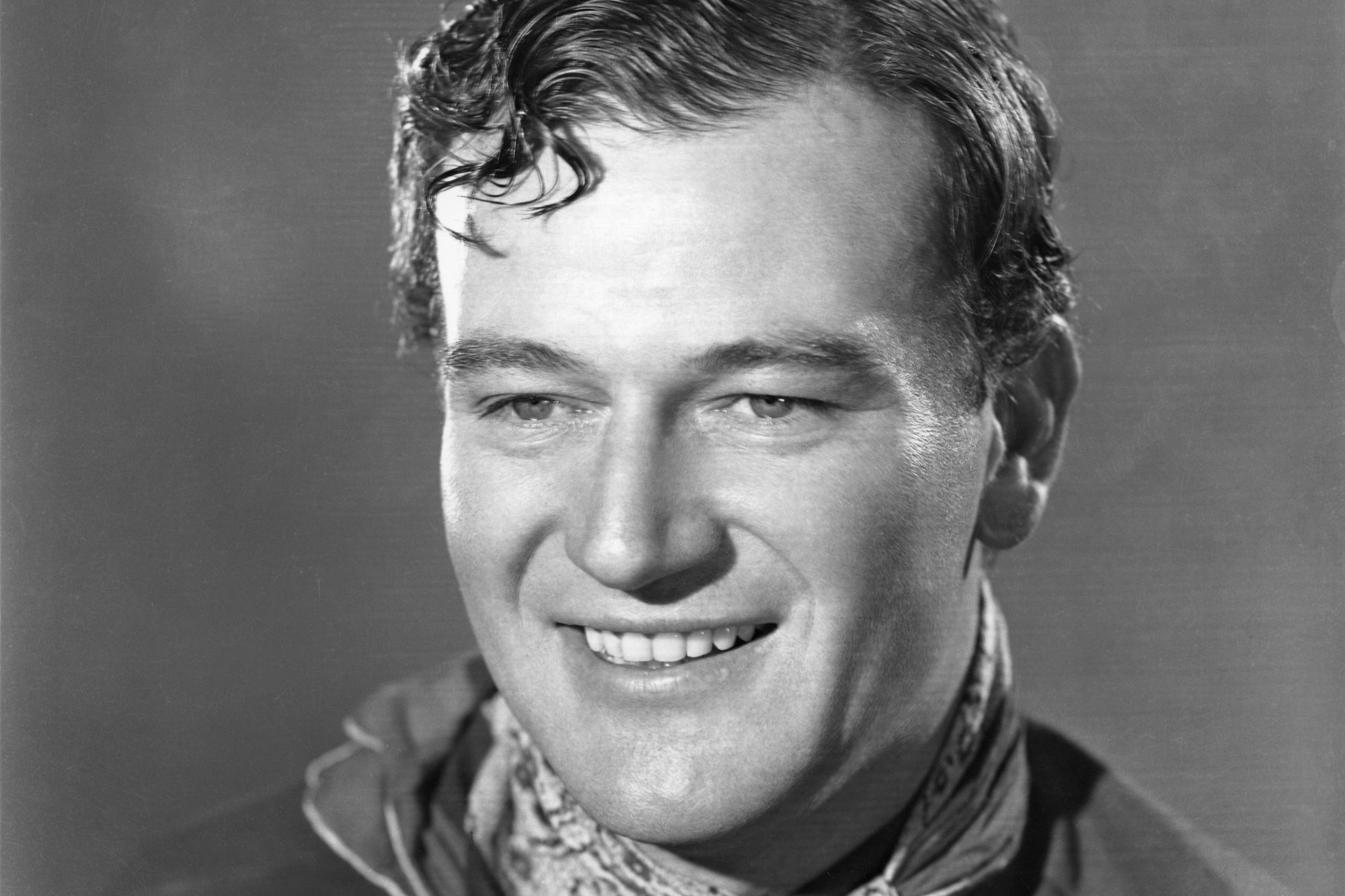 'Stagecoach' actor John Wayne in a black-and-white portrait smiling.