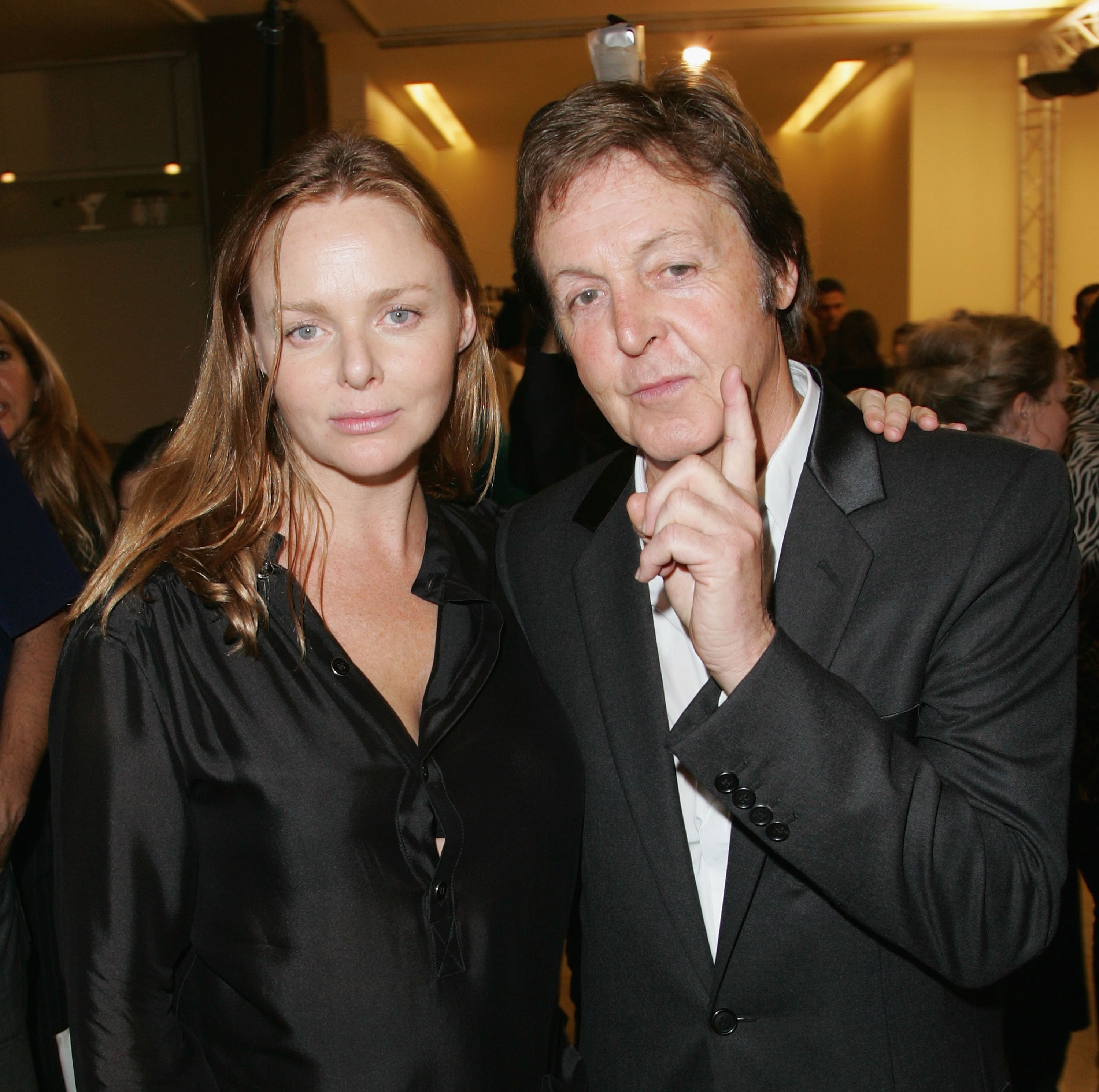 Stella McCartney stands with her arm over Paul McCartney's shoulder.